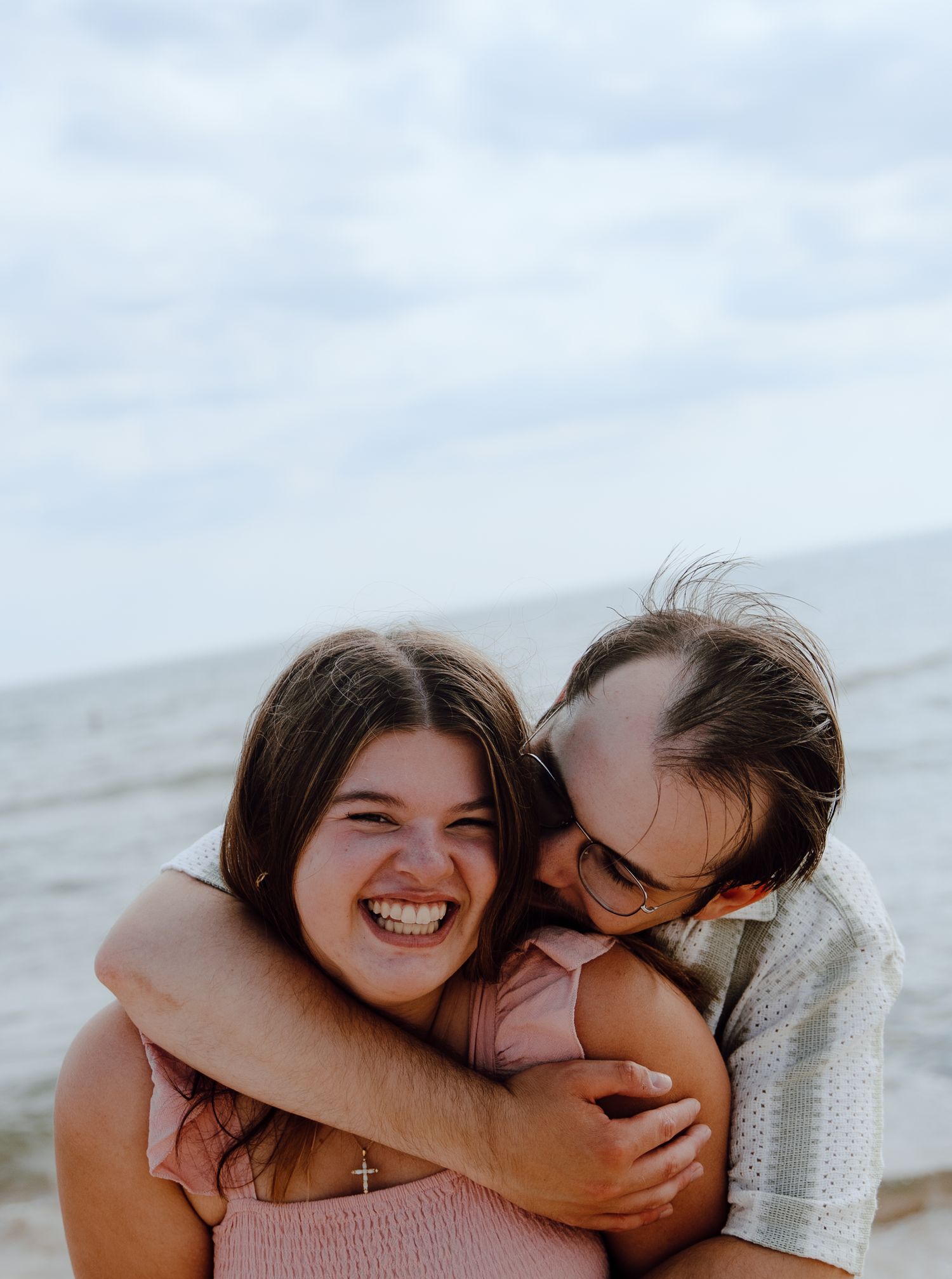 Candid moment of laughter and embrace by the ocean on a cloudy day.