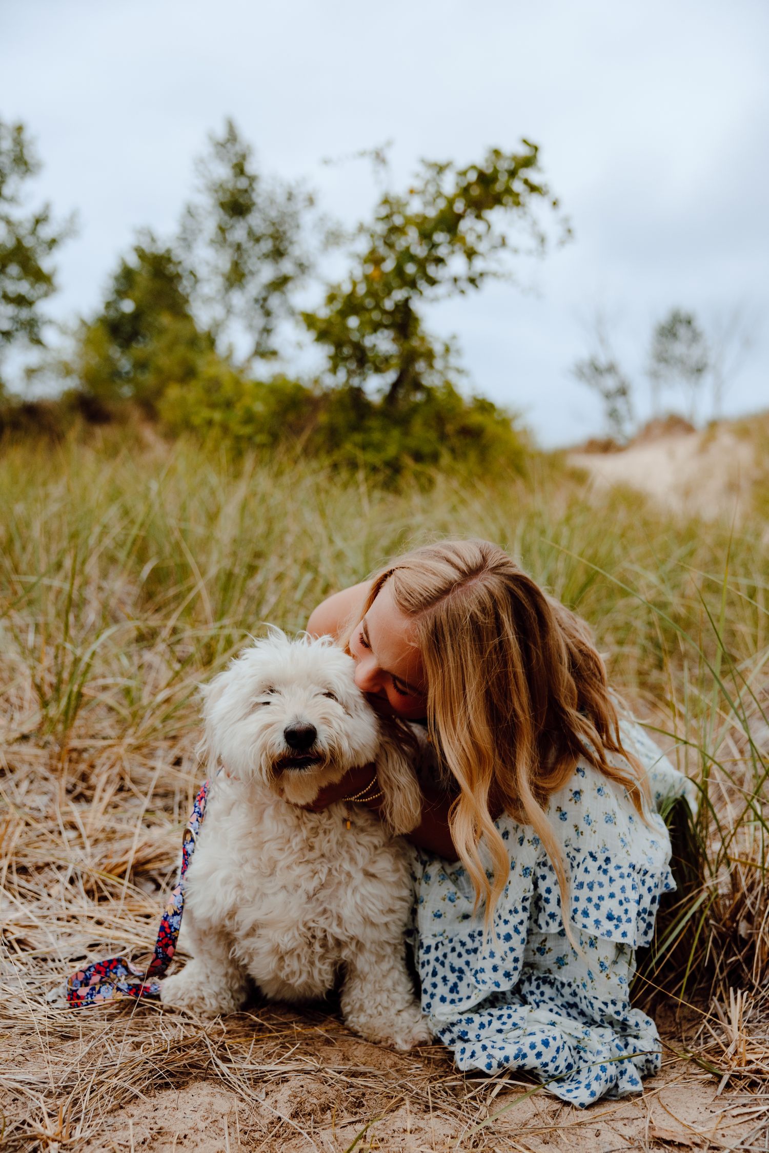 A fluffy white dog and someone in a polka dot dress laying together in a grassy field.