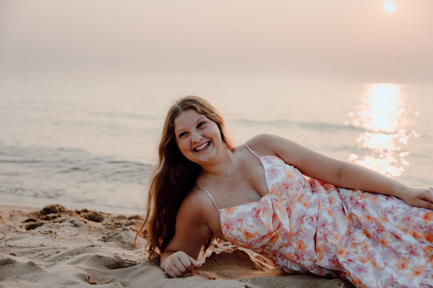 Person in floral dress lying on beach sand during golden hour sunset.