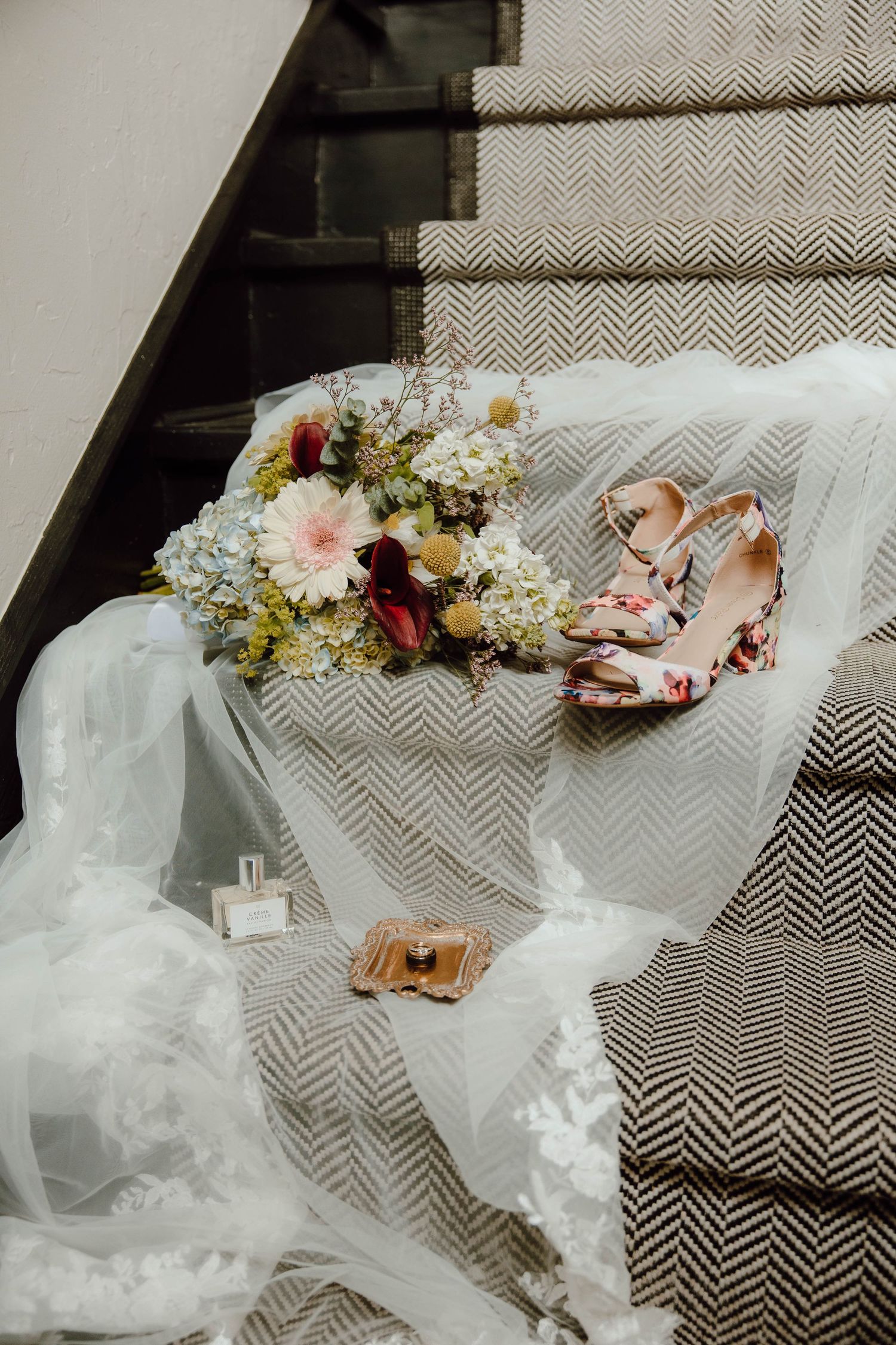 Bridal bouquet with hydrangeas, floral heels, perfume, and veil arranged on herringbone stair runner.