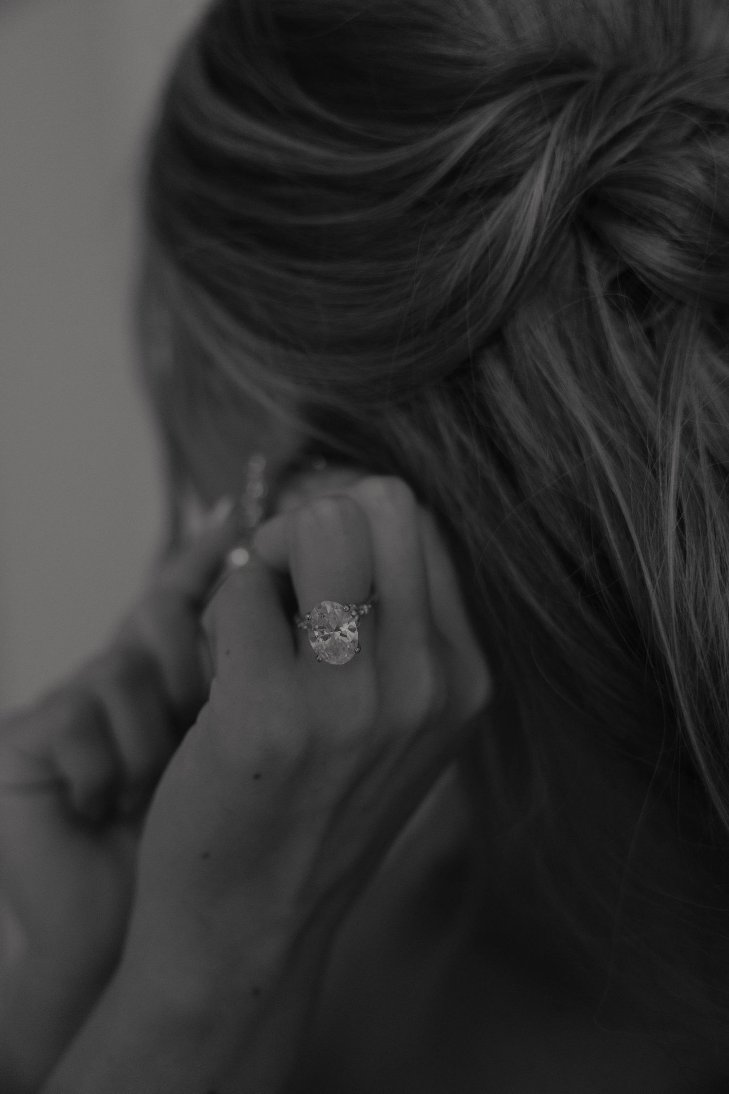 Black and white close-up of bride adjusting earring with a stunning diamond engagement ring on her hand.