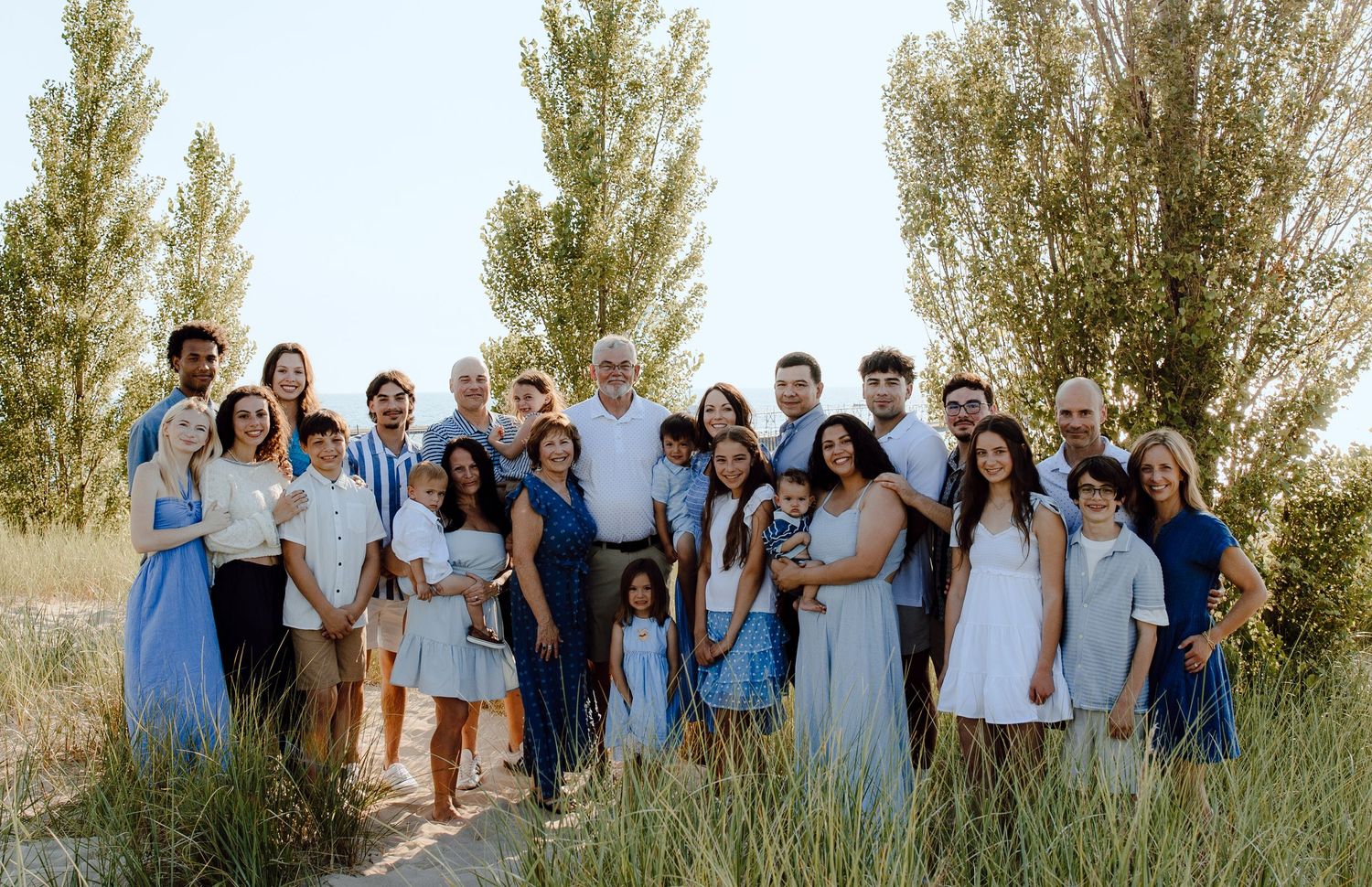 Large group wearing blue and white outfits poses together among tall beach grass.