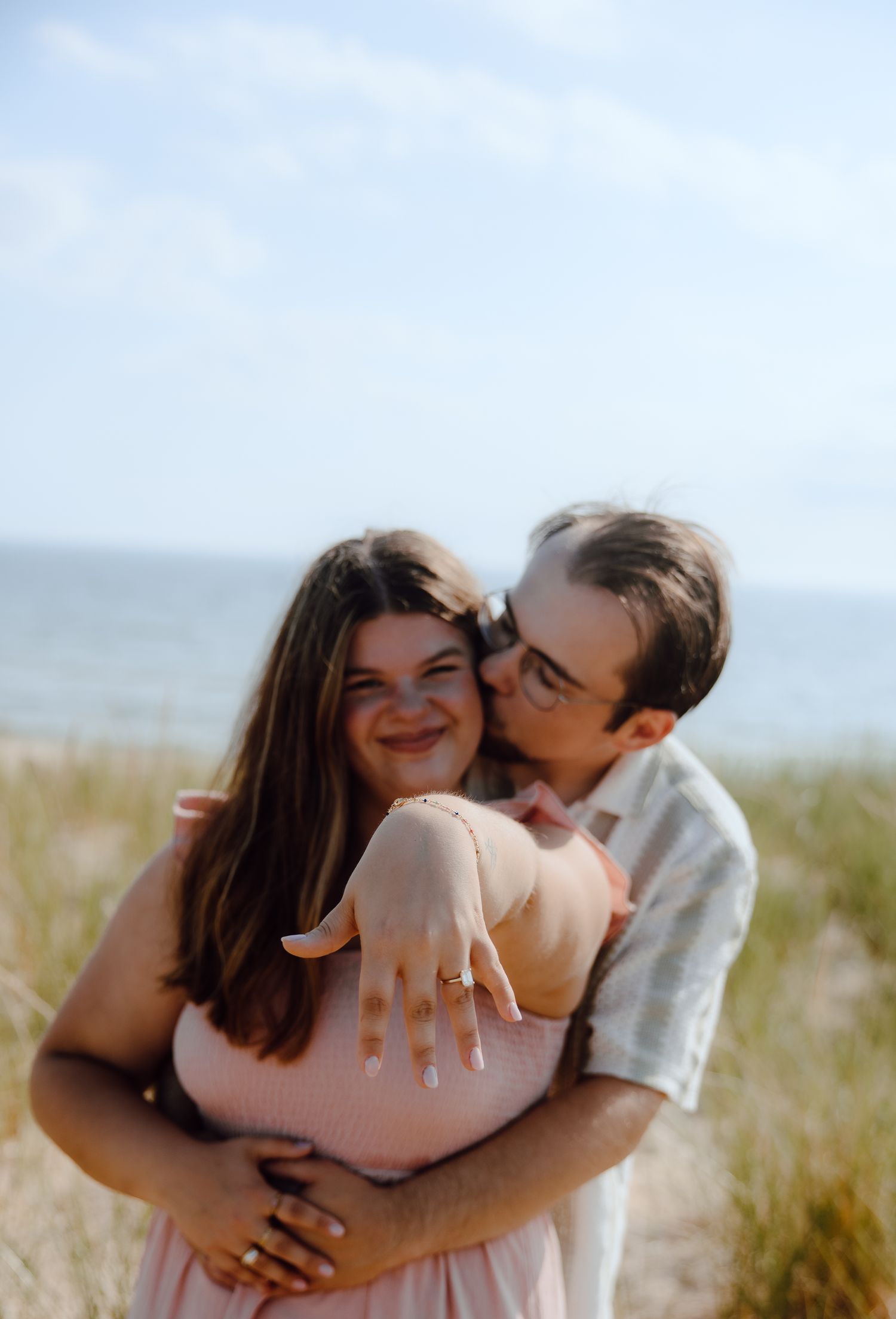 A joyful embrace captured among beach grass with ocean views.