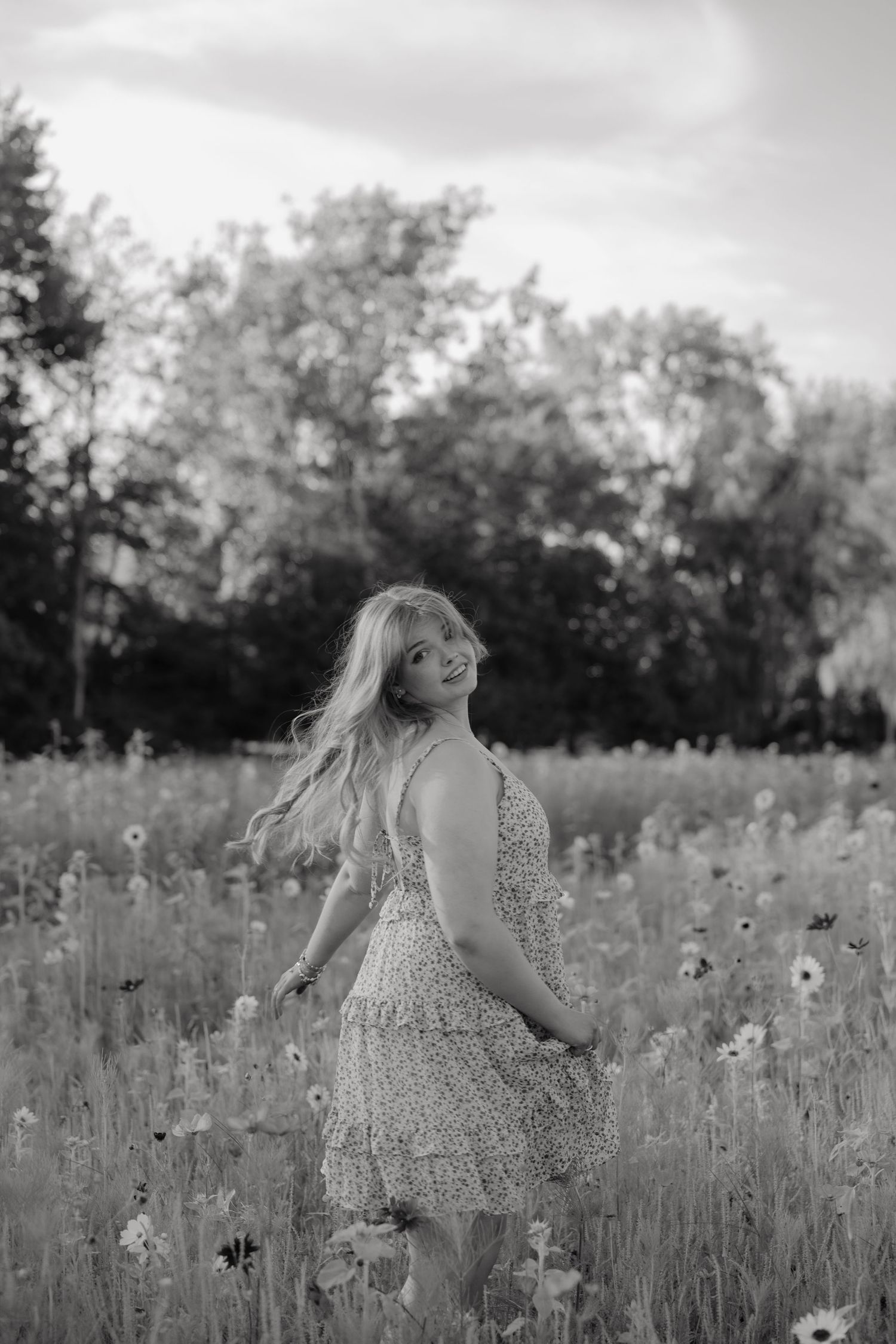 Black and white portrait of blonde girl in floral dress twirling in wildflower meadow.