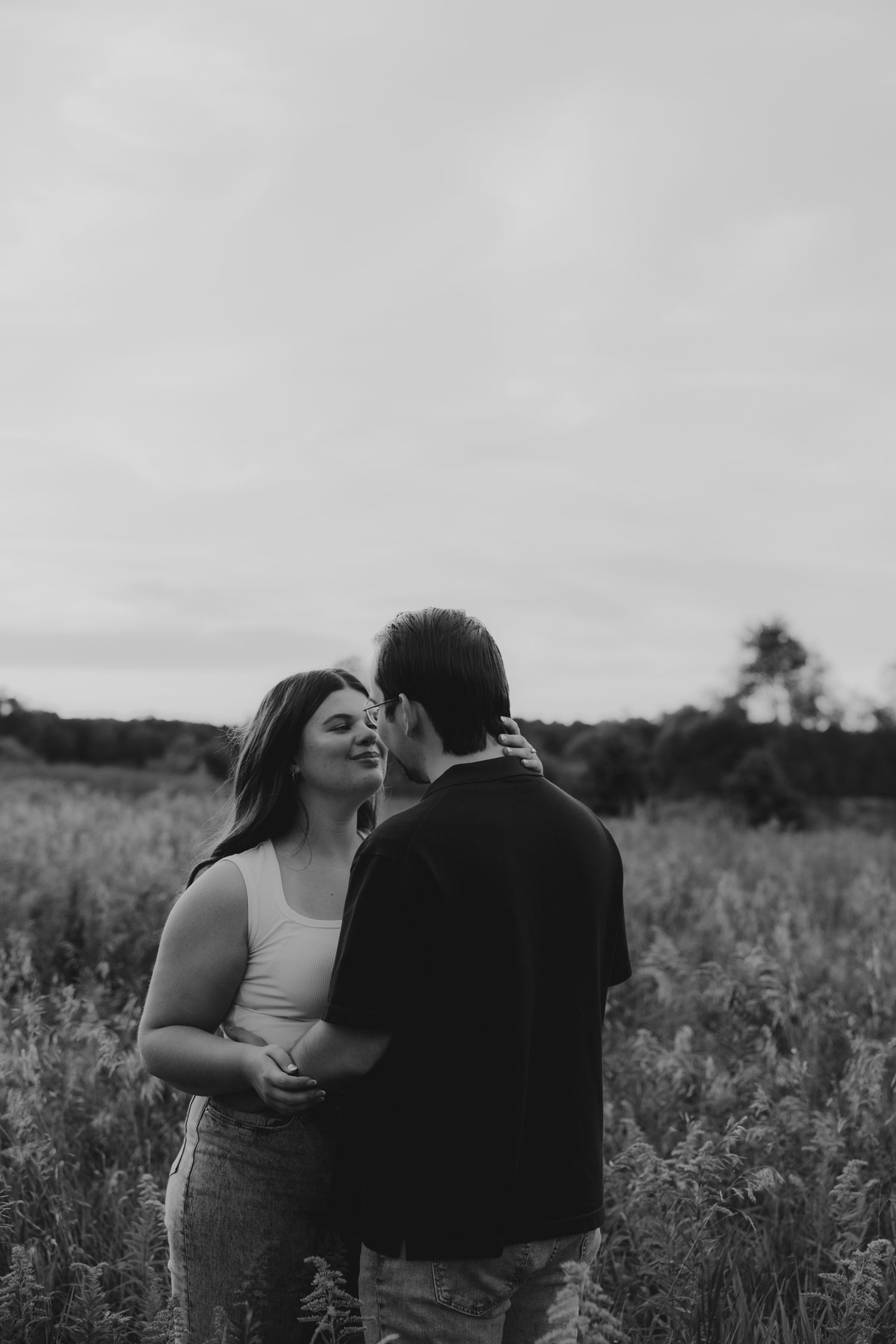A romantic couple shares an intimate moment in a wildflower field at sunset in black and white.