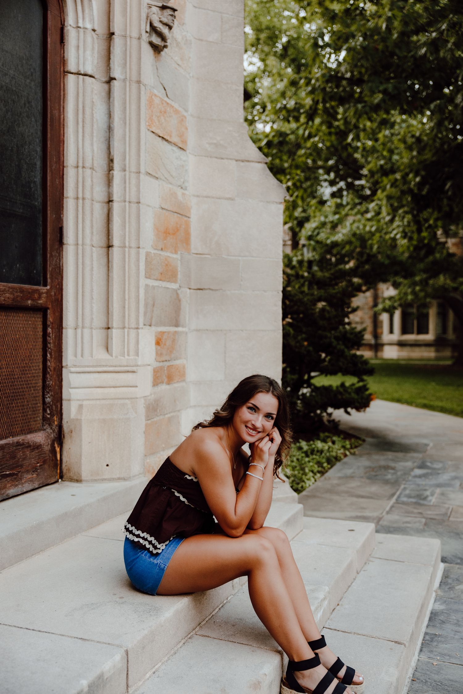 A person in casual attire poses on stone steps against a Gothic architectural backdrop.