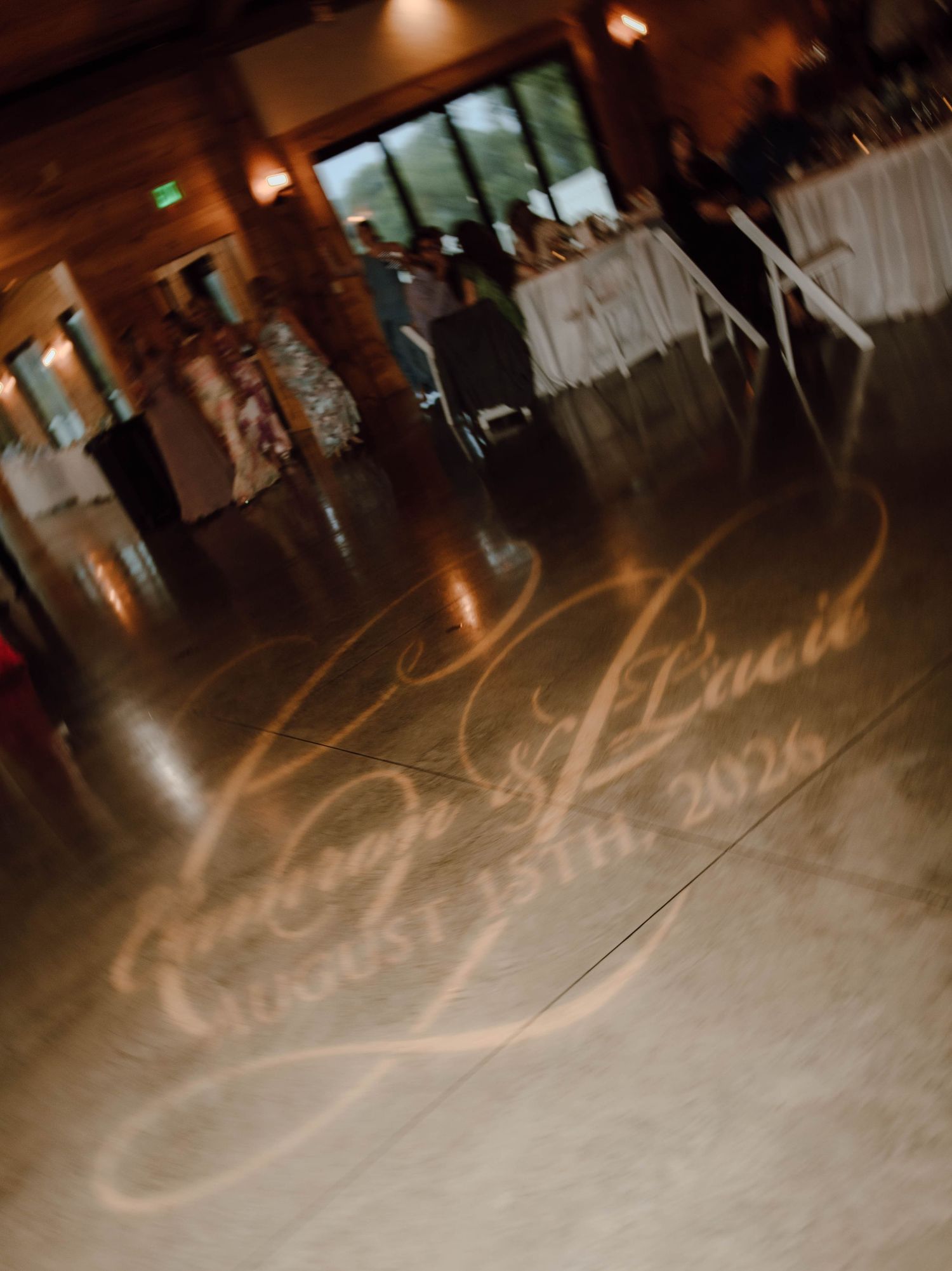 Romantic dance floor monogram light projection displaying couple's names and August 13th 2026 wedding date.