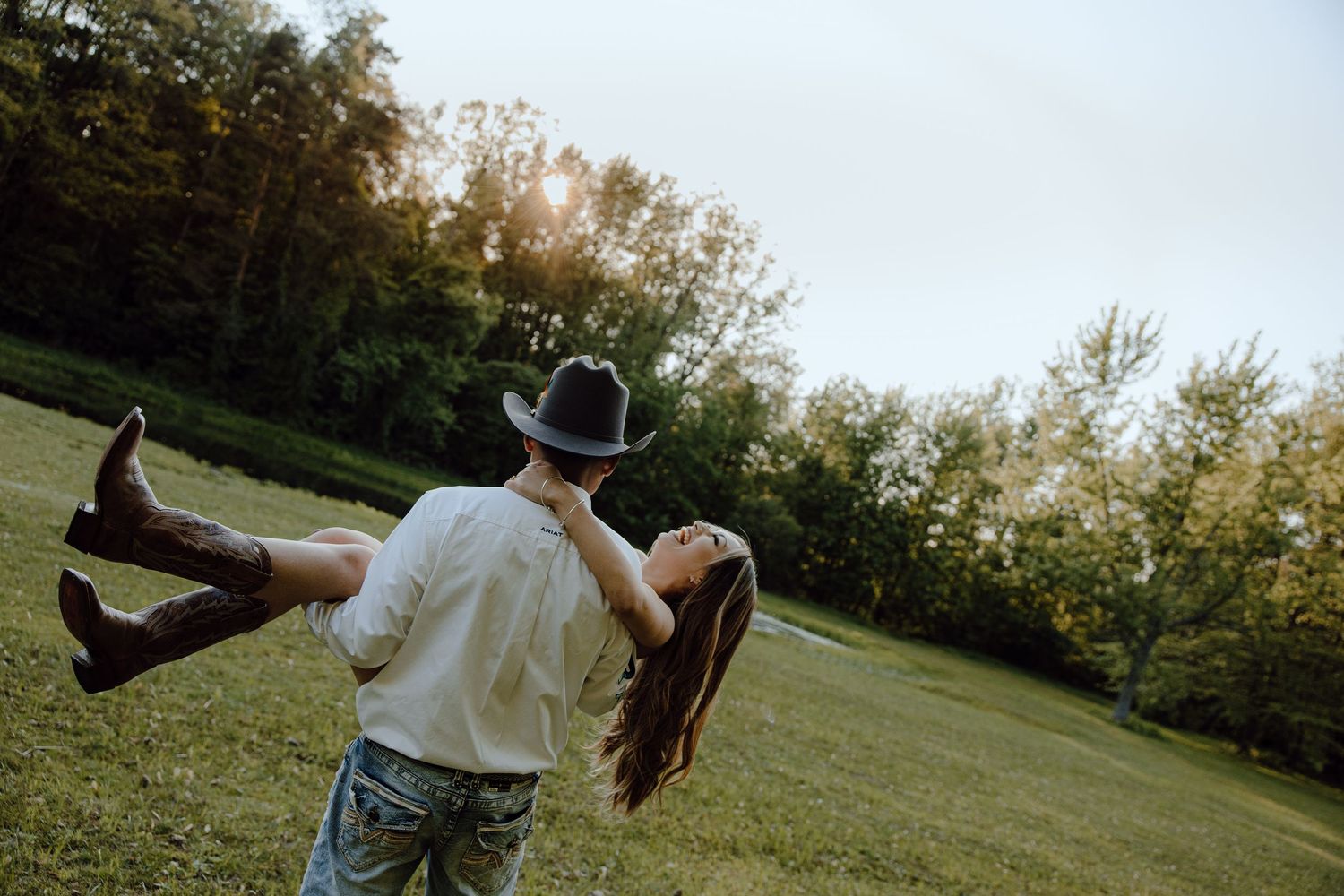A couple shares a romantic moment on a white fence in a sunlit field.
