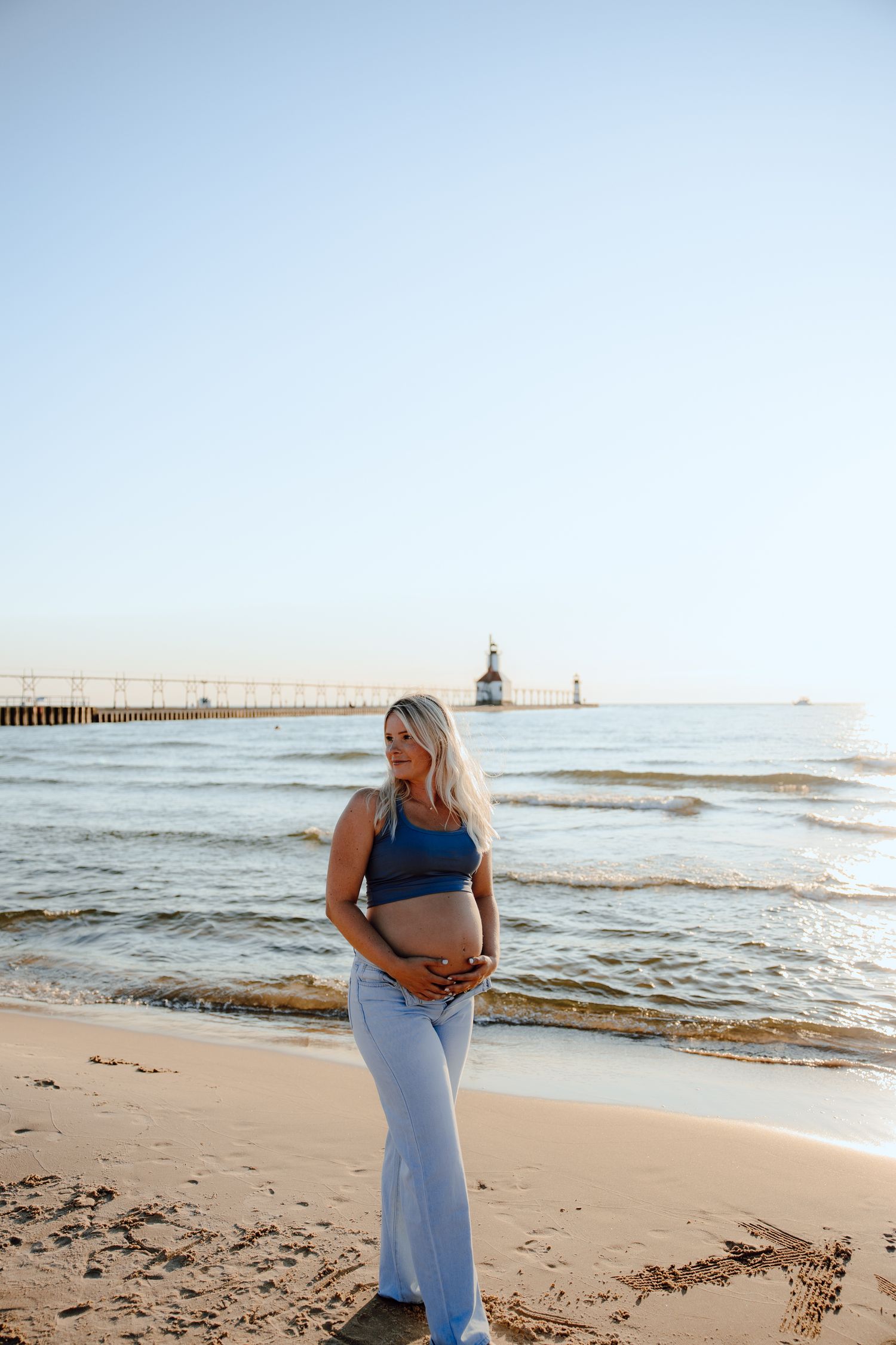 Maternity photos on beach with lighthouse and ocean waves in background.
