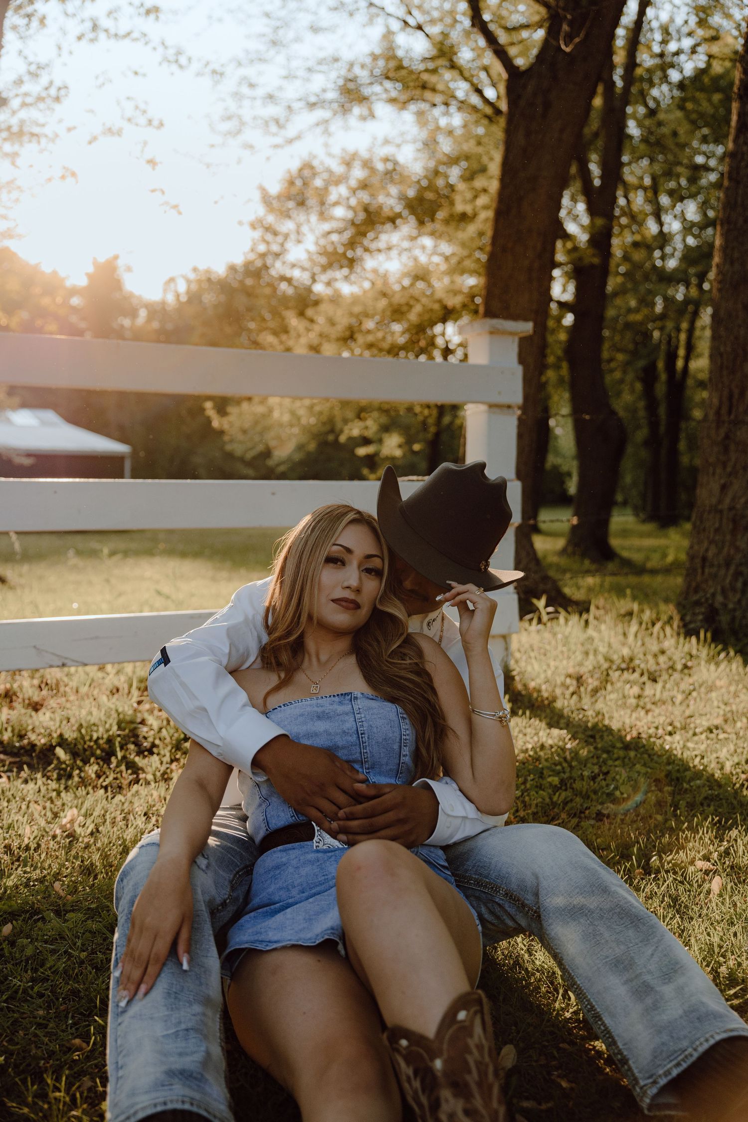 Two people share an intimate moment while resting against a white fence at golden hour.