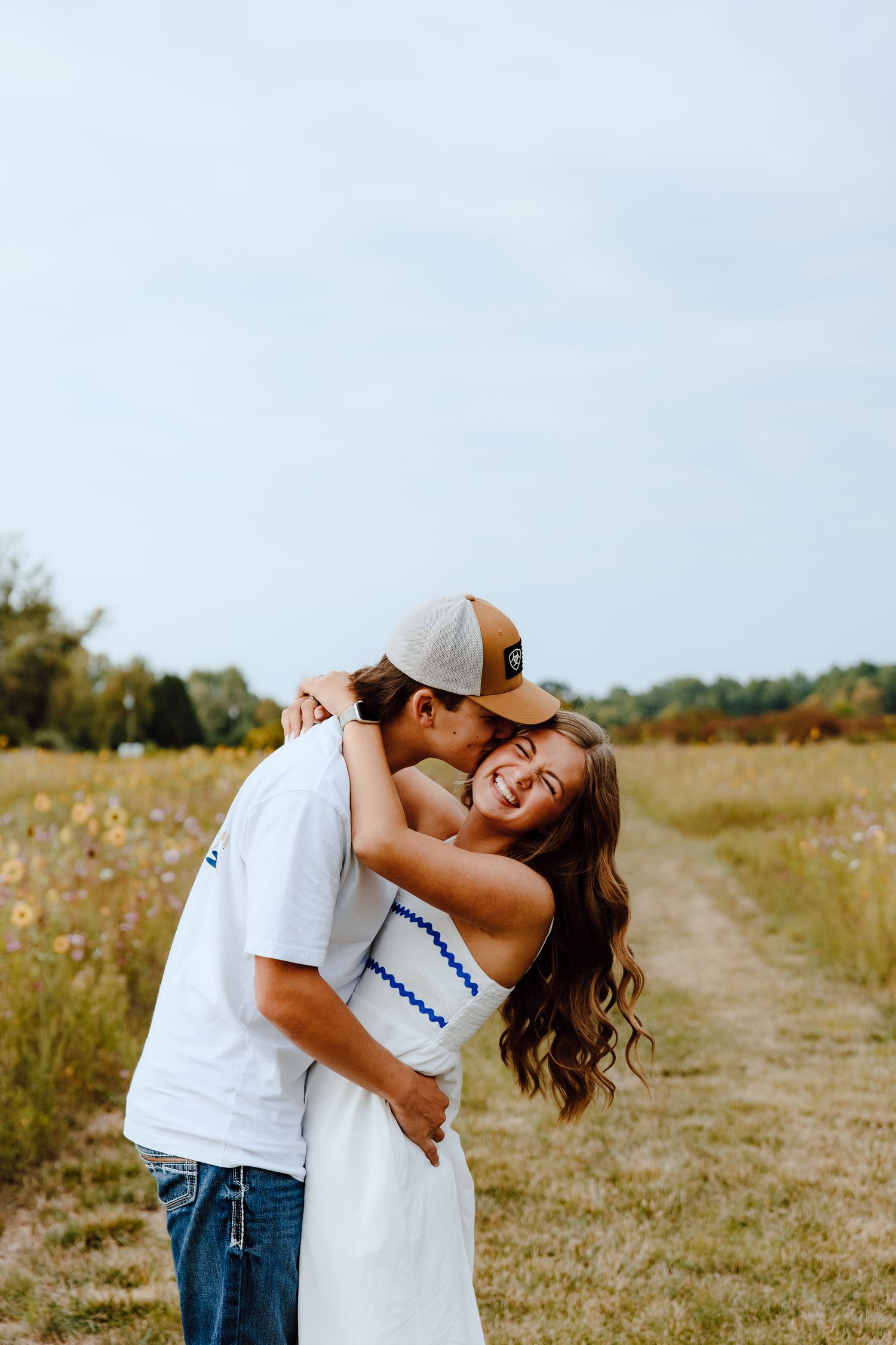A playful couple shares a romantic moment on a path through a summer meadow.