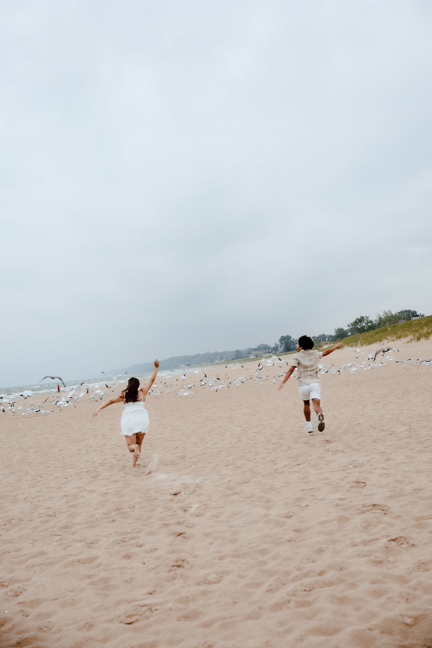 People playing and running on a sandy beach with seagulls flying overhead.