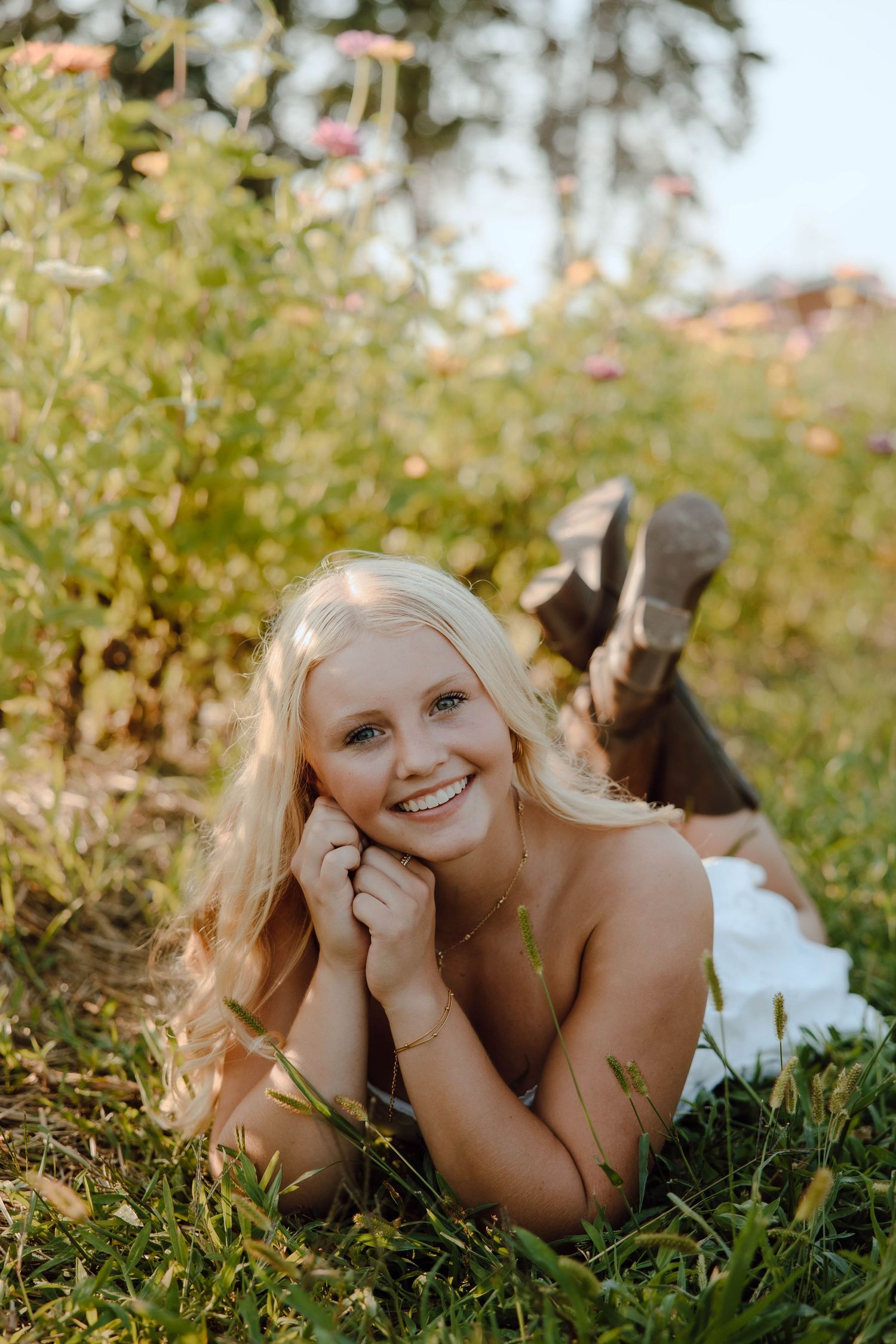 Smiling blonde woman lying in green grass surrounded by wildflowers on a sunny day.
