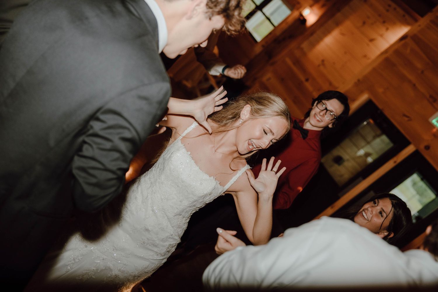 Bride in white lace dress dancing energetically with guests at wedding reception.