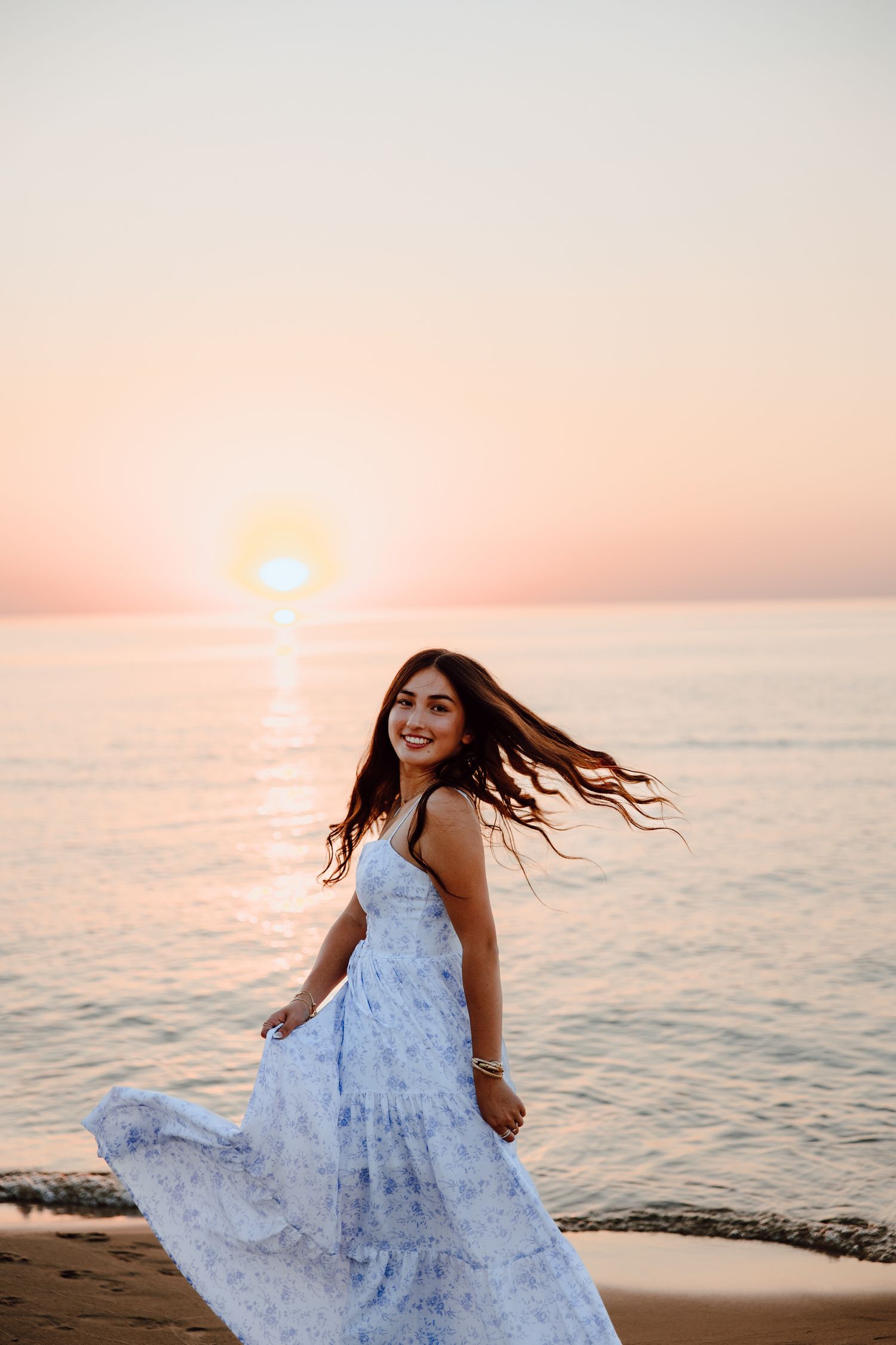 Woman in flowing blue dress twirling on beach at sunset.