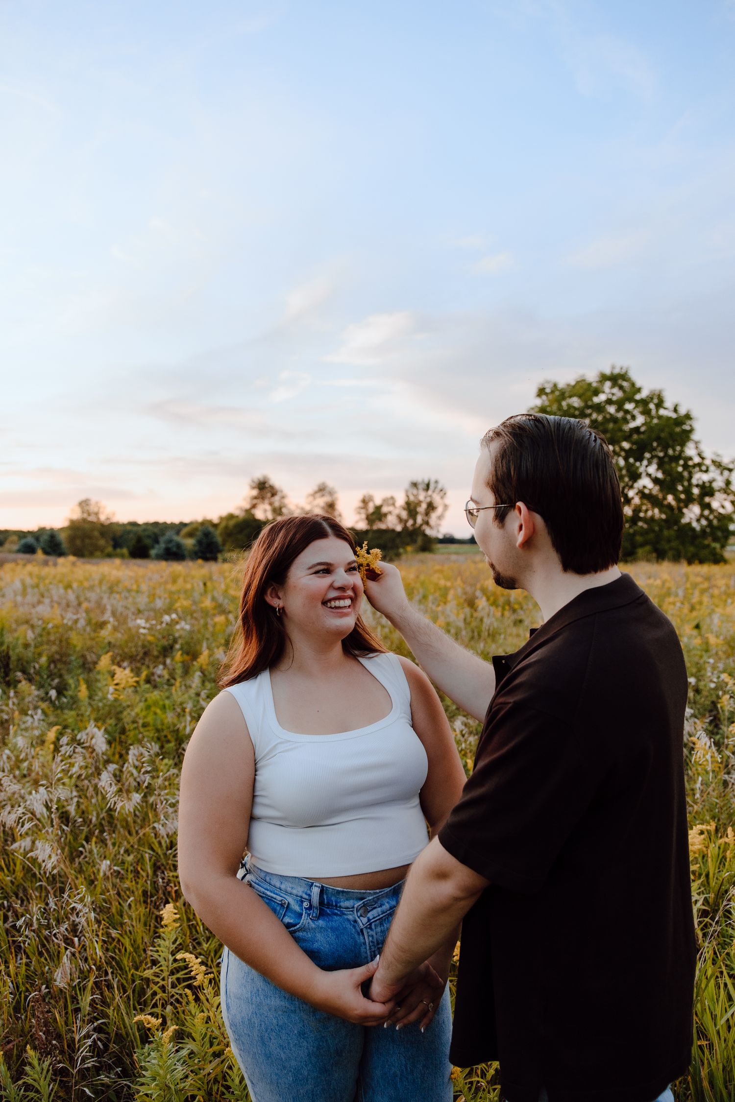 A couple laughs together while standing in a field of wildflowers at dusk.