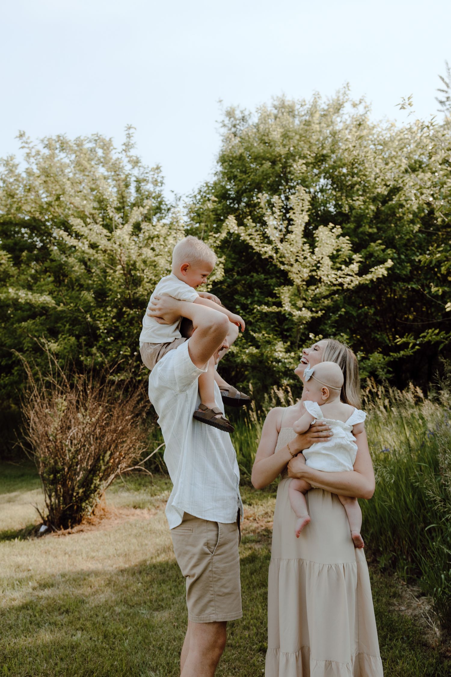A playful family photo sequence showing parents tossing their baby in the air in a sunny outdoor garden setting.