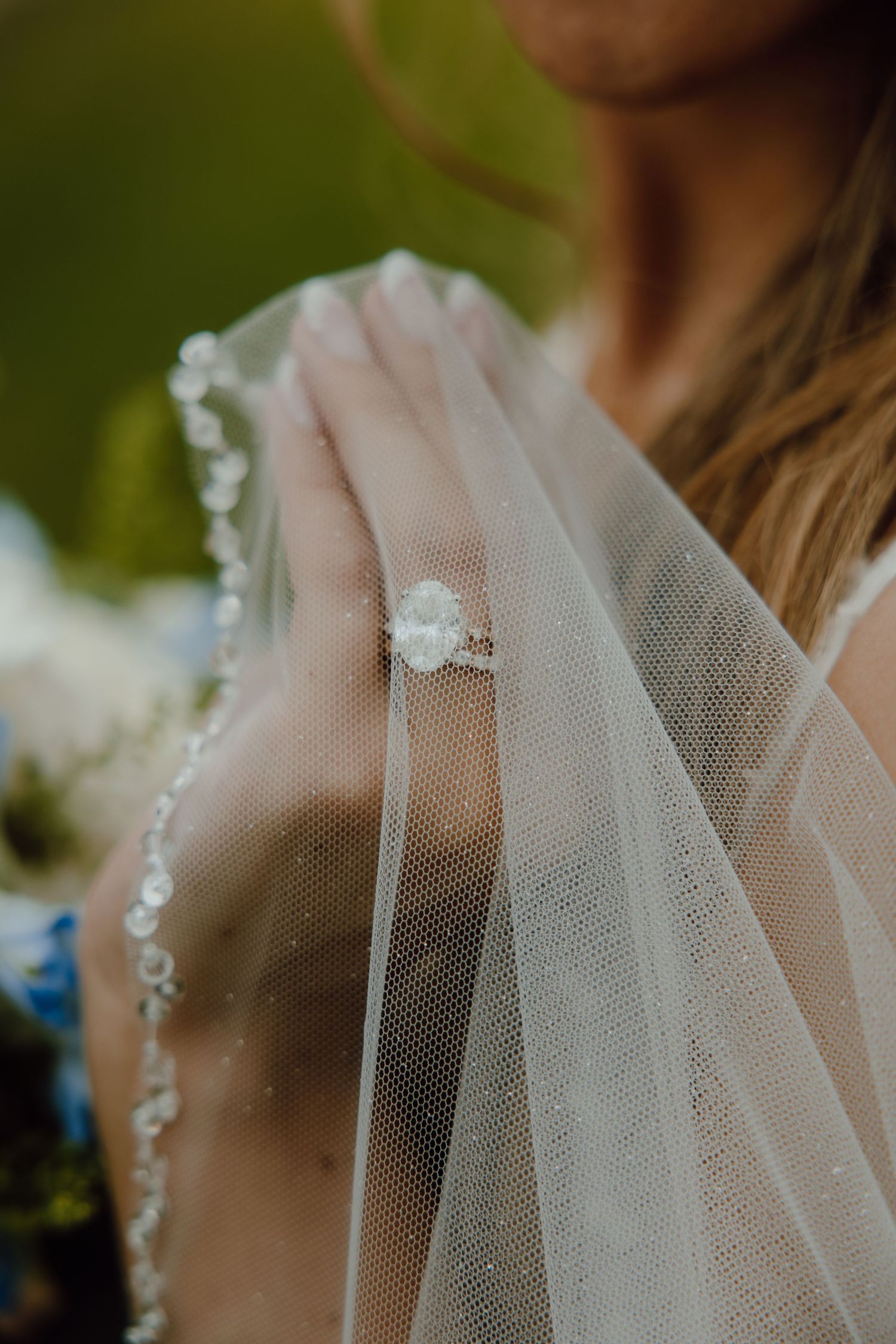 Bride showcasing an oval diamond engagement ring draped with a delicate lace-trimmed wedding veil.