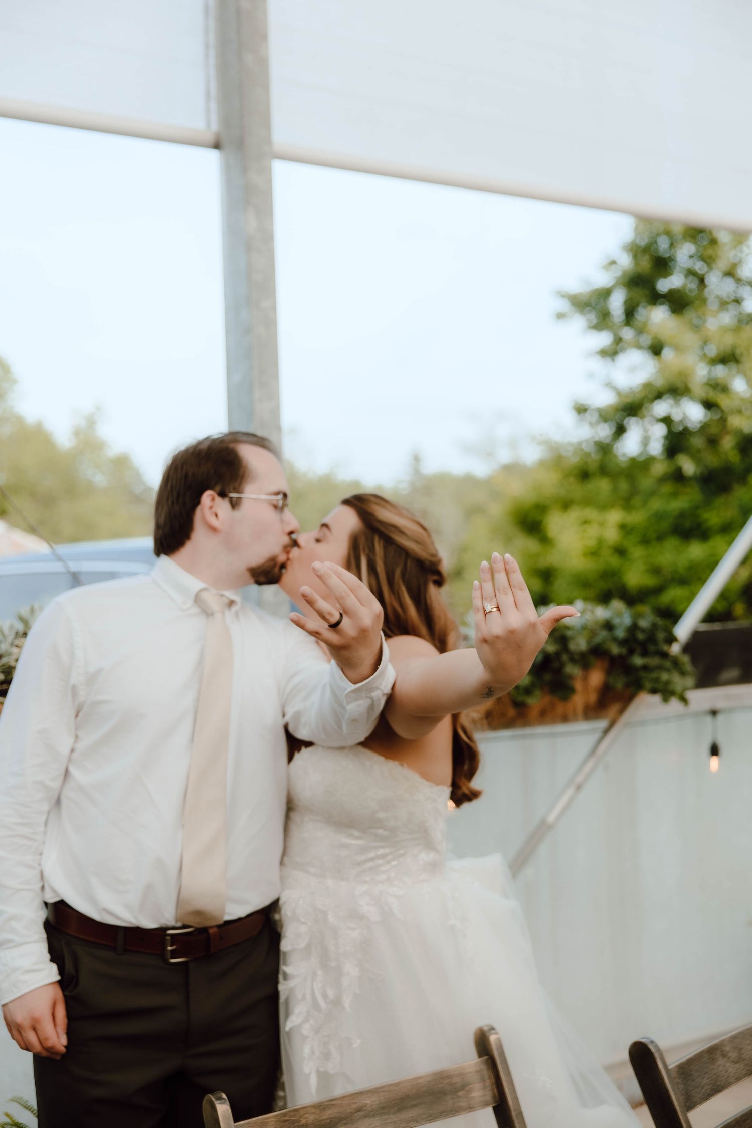 Bride and groom kiss while showing off wedding rings at indoor wedding reception.