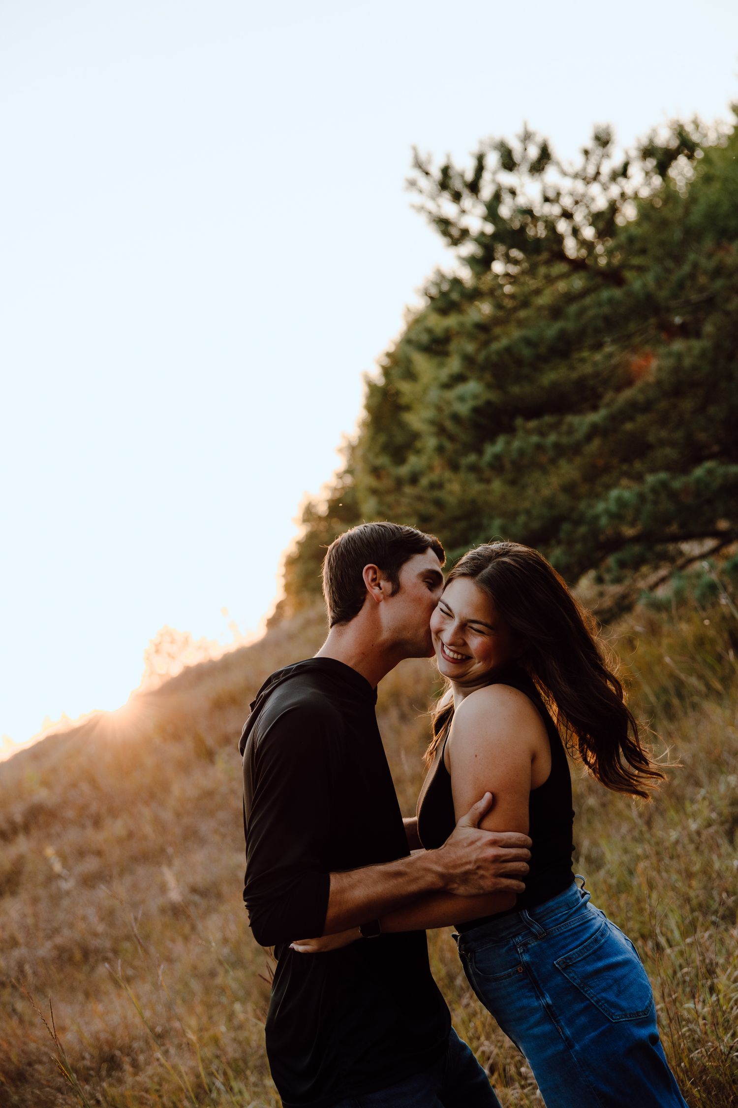 Couple shares intimate moments on a grassy hillside during sunset.