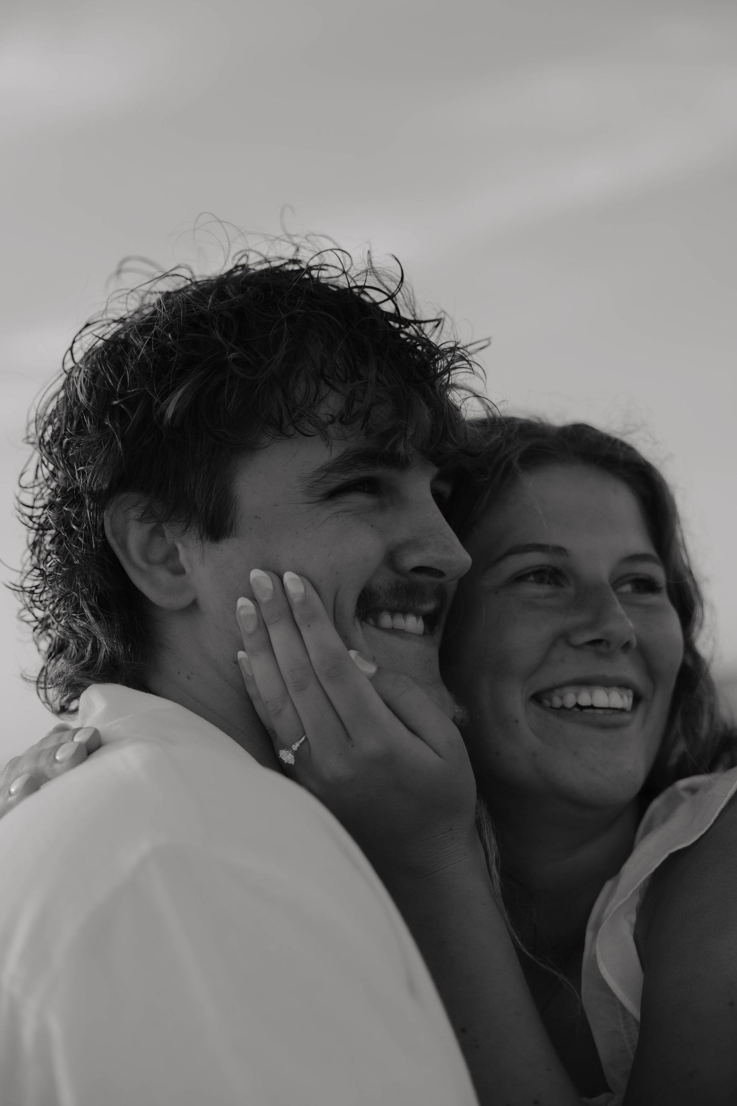 Black and white photo of a smiling couple, woman resting hand on mans cheek, both looking up joyfully.