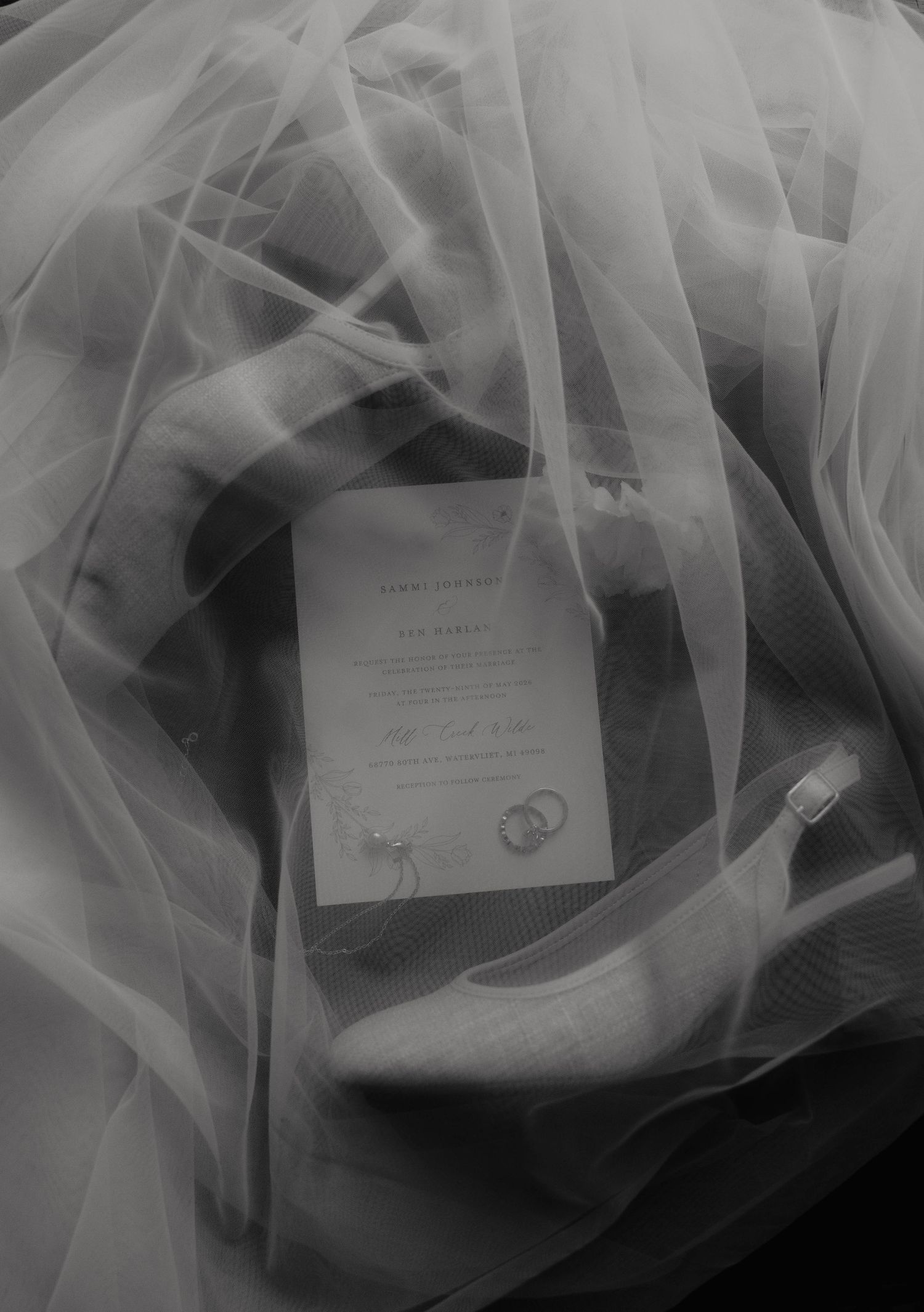 Black and white wedding flat lay with invitation, rings, and bridal veil draped elegantly over accessories.