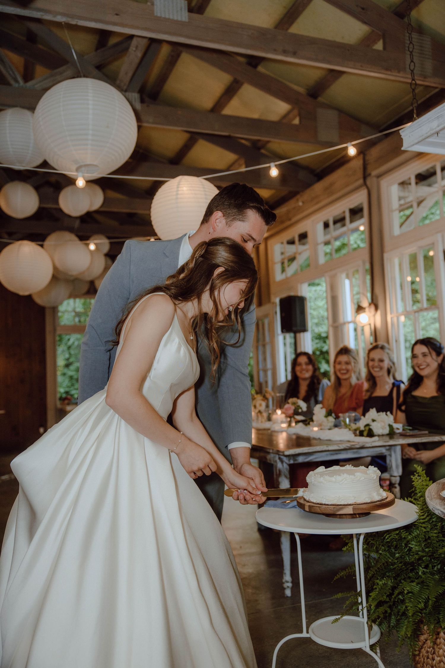 Bride and groom cut their white wedding cake together under paper lanterns at an elegant reception.