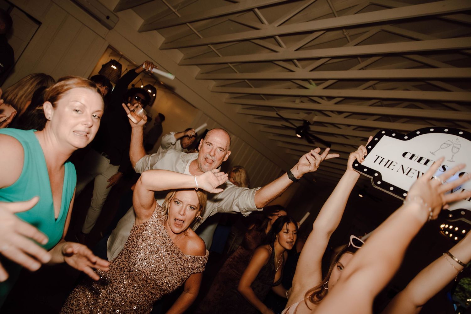 Guests dancing and celebrating at a lively wedding reception party with raised arms and joyful expressions.