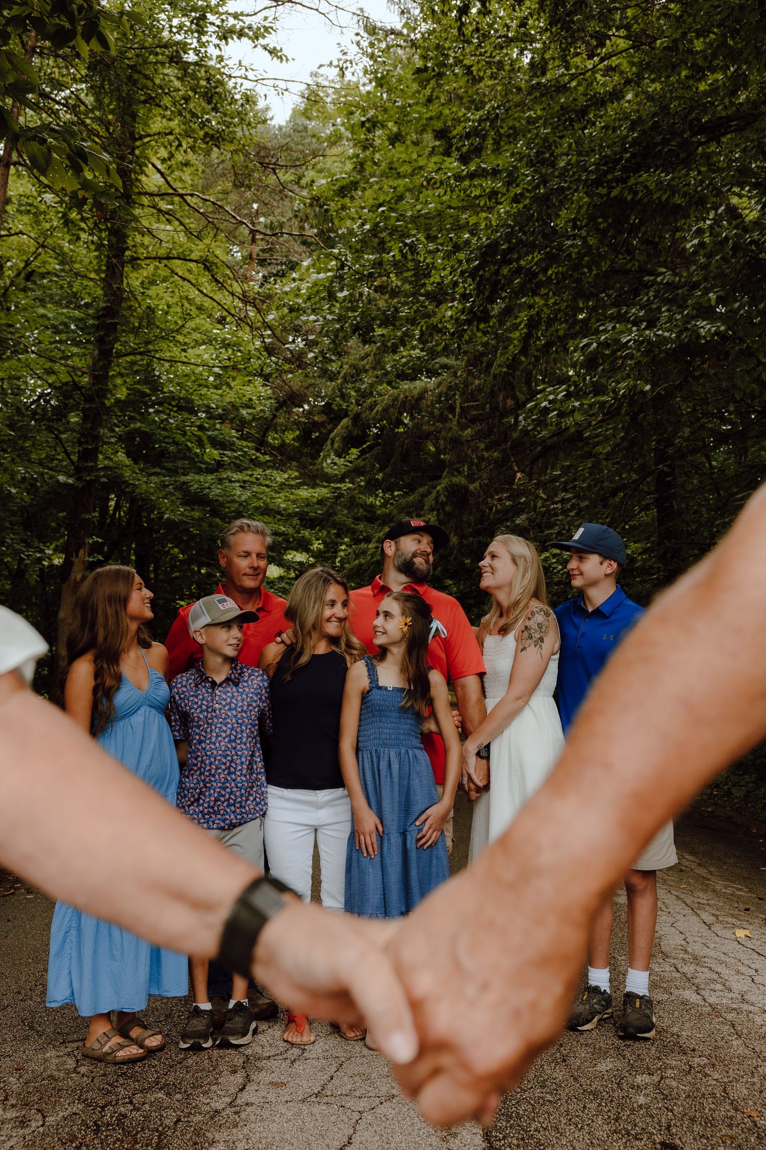 Family members hold hands in a line while standing together on a wooded path.