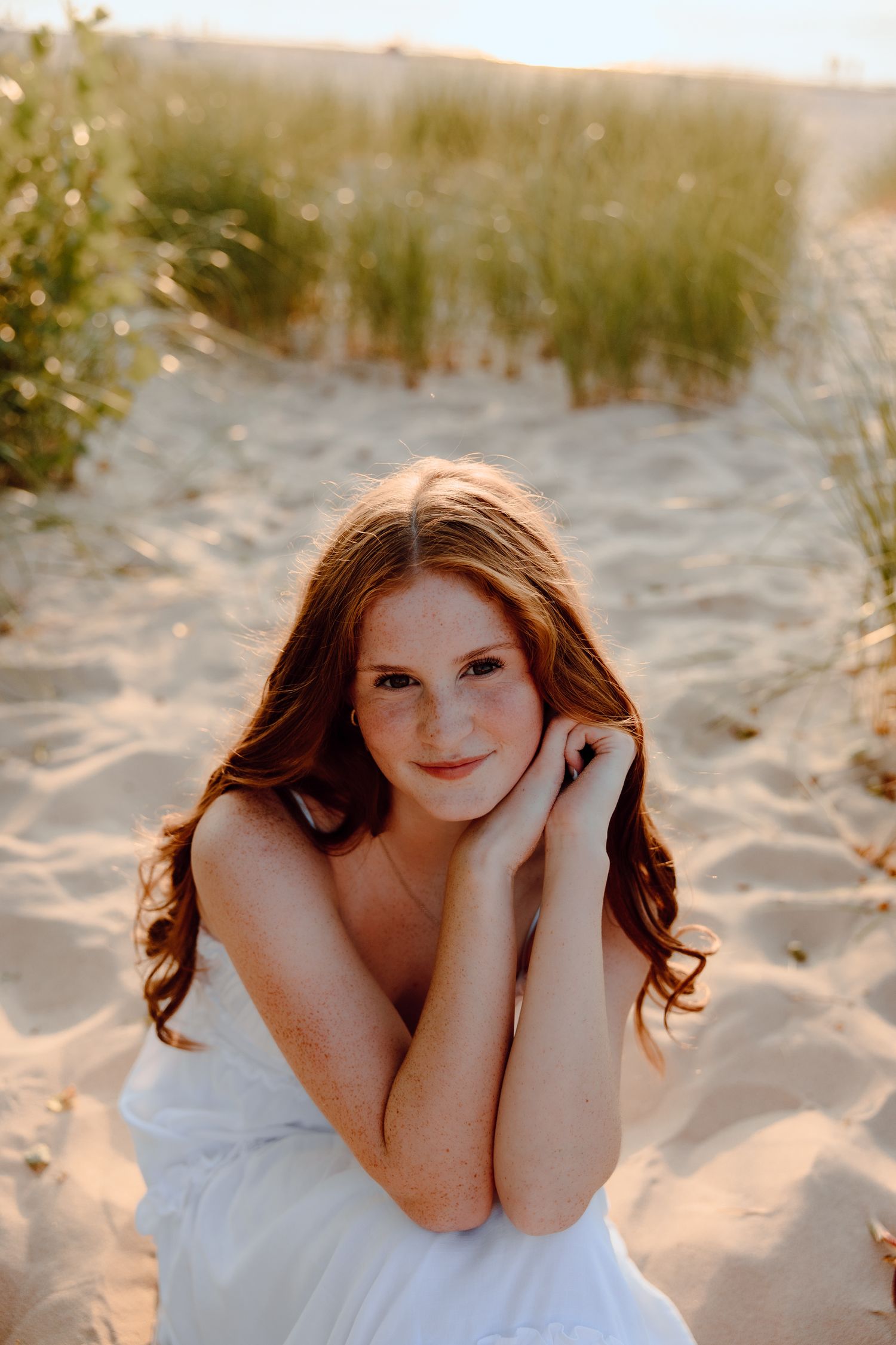 Someone in a white dress poses on sandy dunes at sunset.