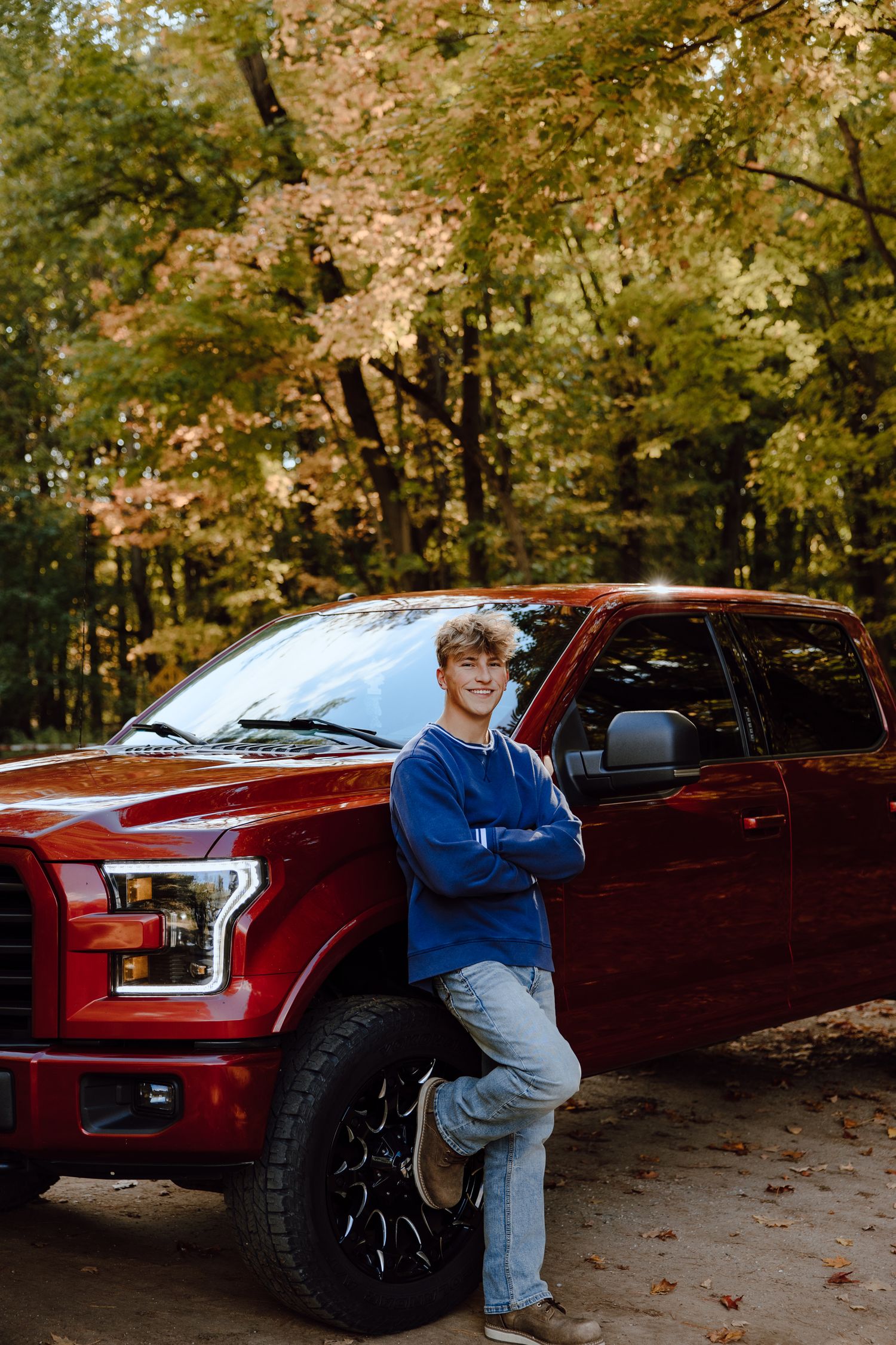 Athletic senior portrait with red Ford pickup truck against autumn foliage background.