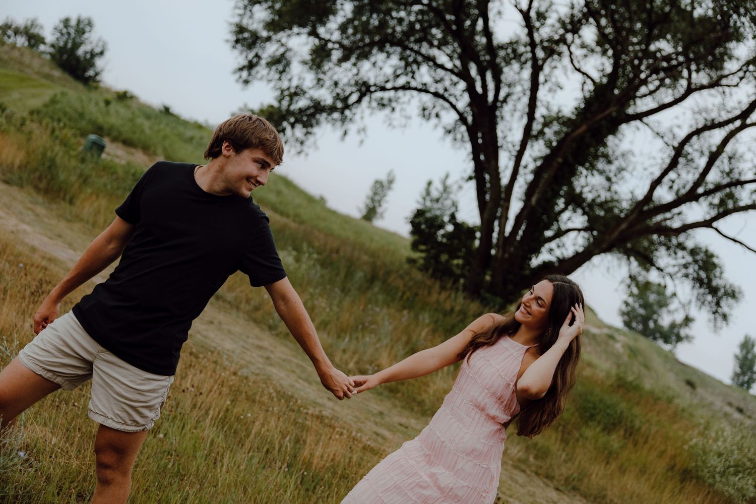 A couple dances playfully in a grassy field during golden hour.
