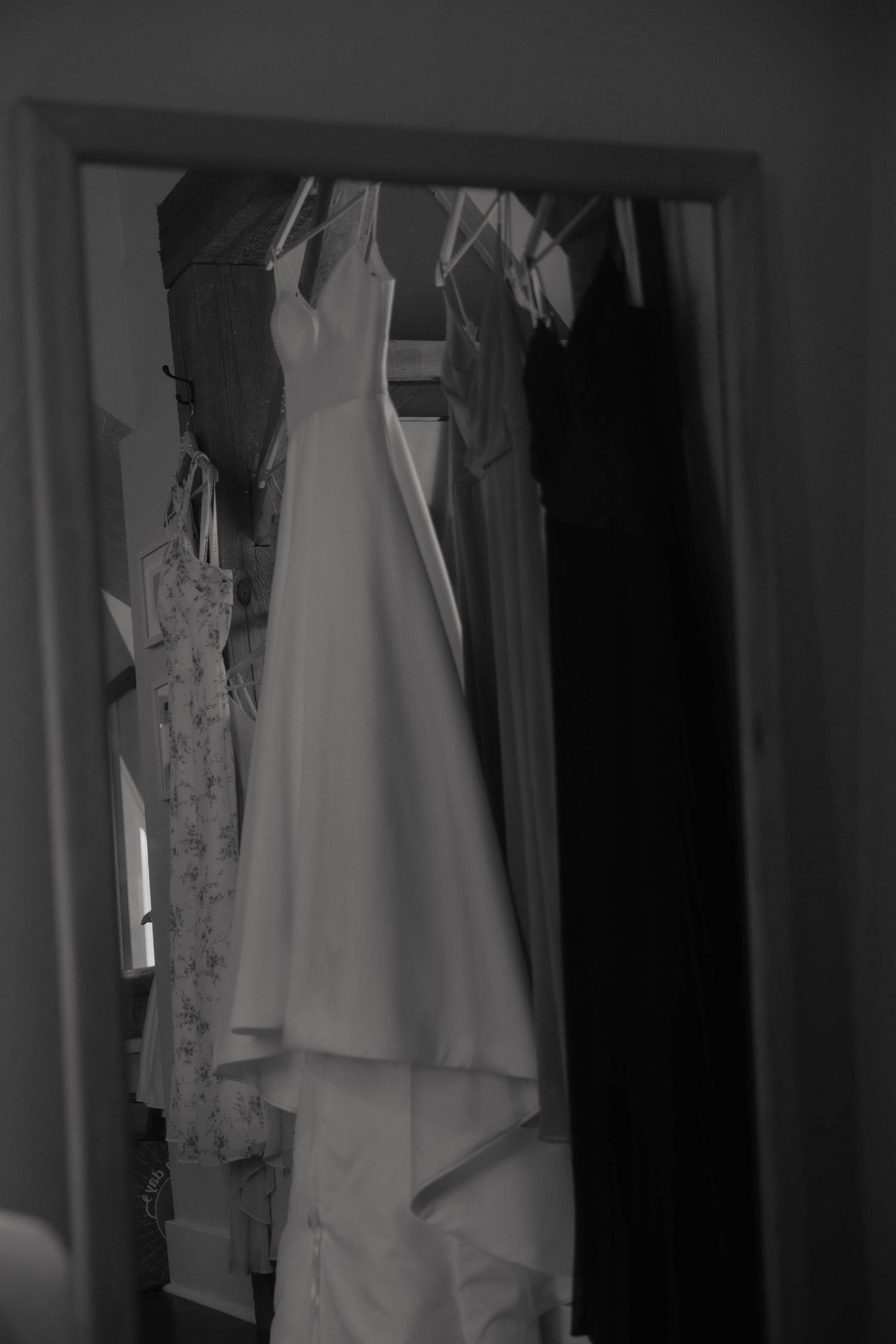 Black and white photo of a white wedding dress hanging in a closet doorway.