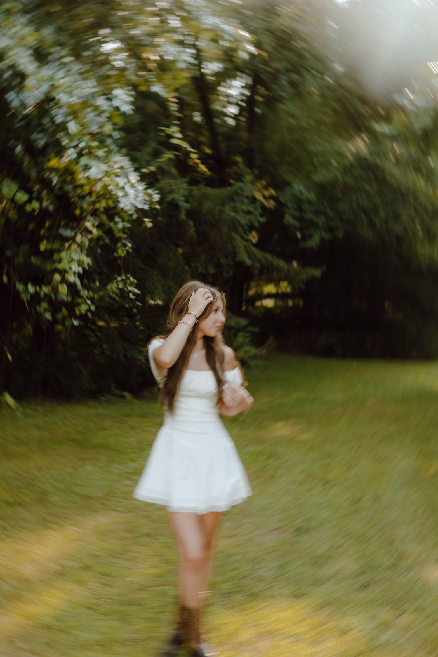 Young woman in white dress posing gracefully in a lush green garden with artistic blur effect.