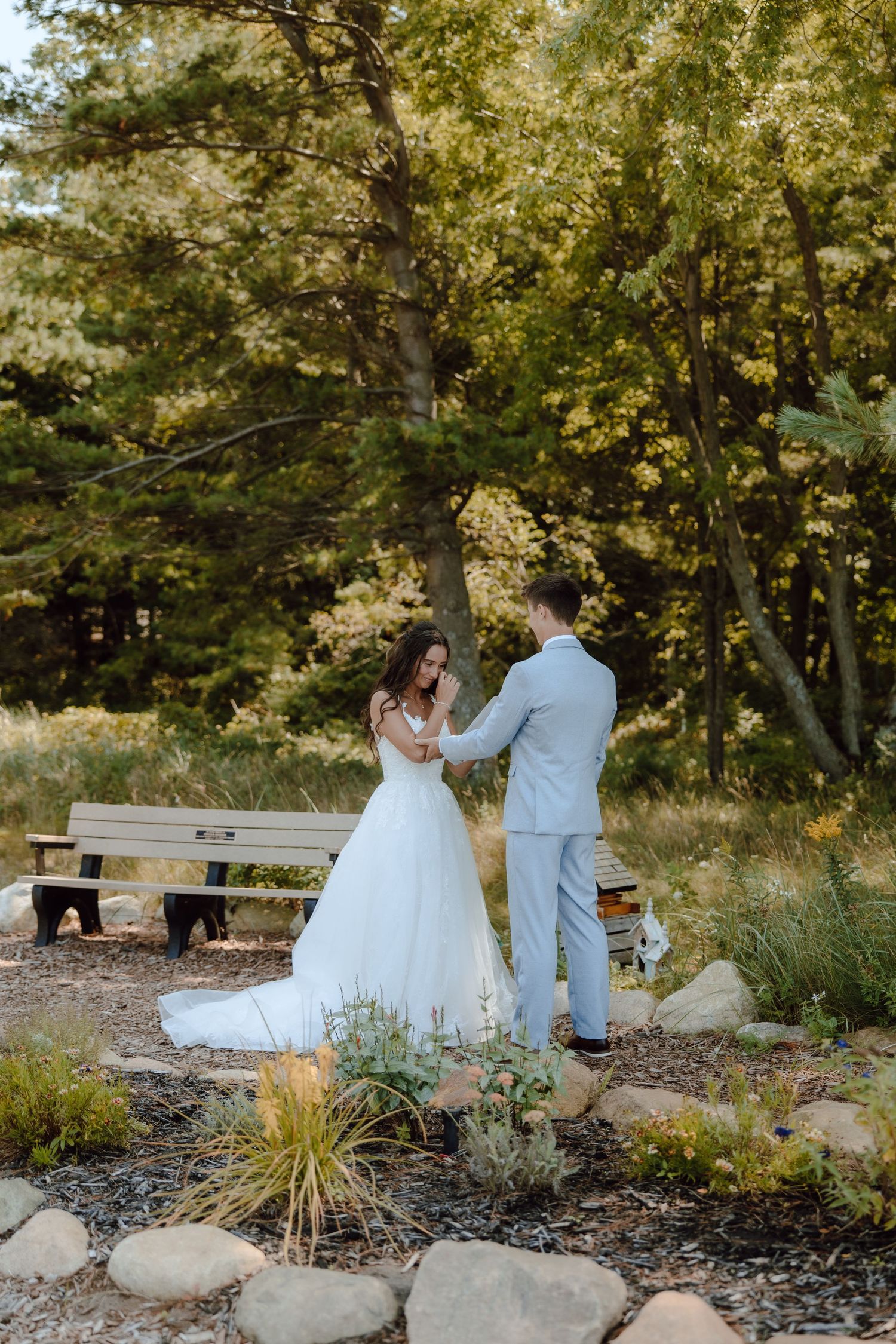 Bride and groom share a tender moment holding hands in a lush garden setting during their outdoor wedding ceremony.