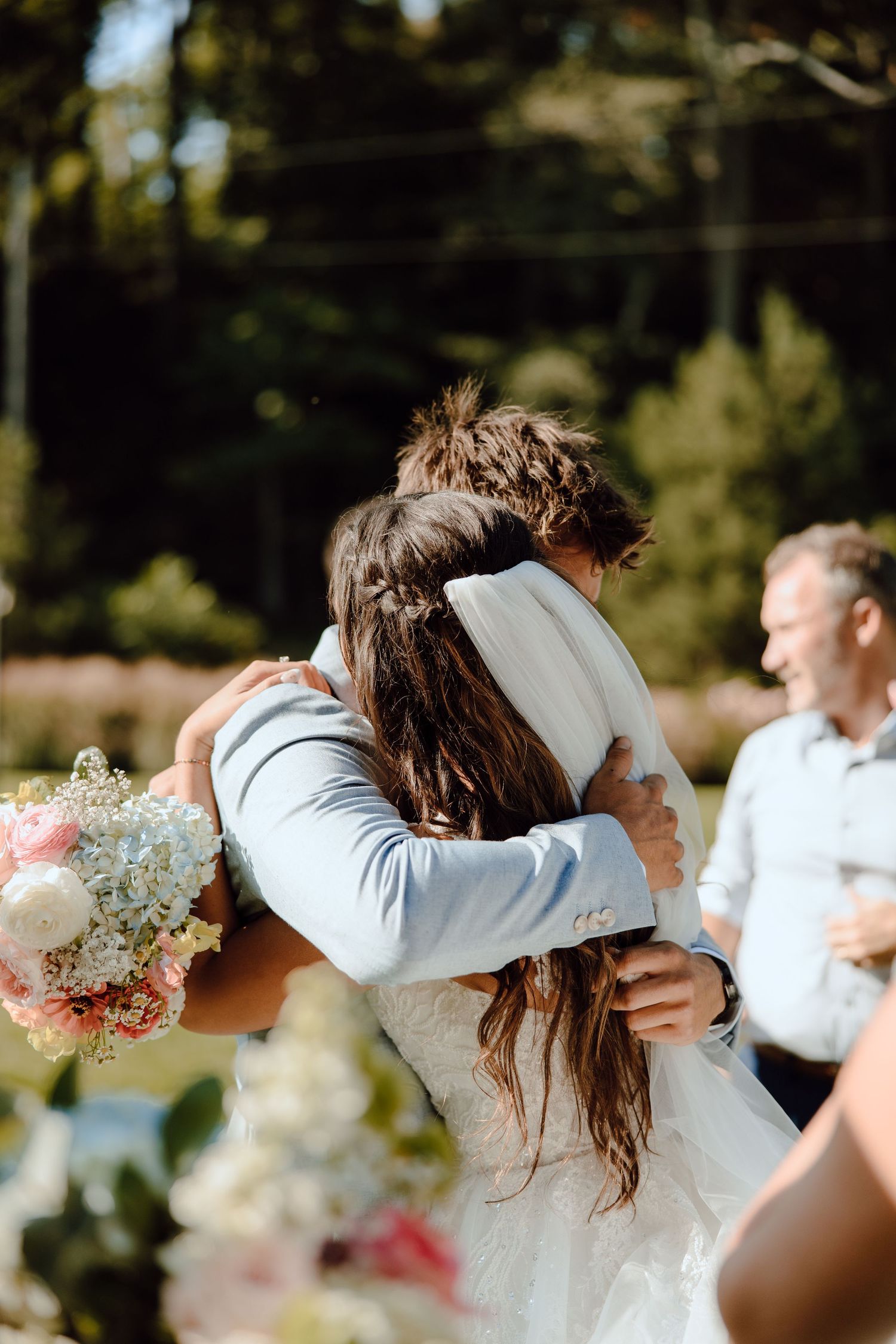 Bride and groom share an emotional embrace during outdoor wedding ceremony with bouquet.