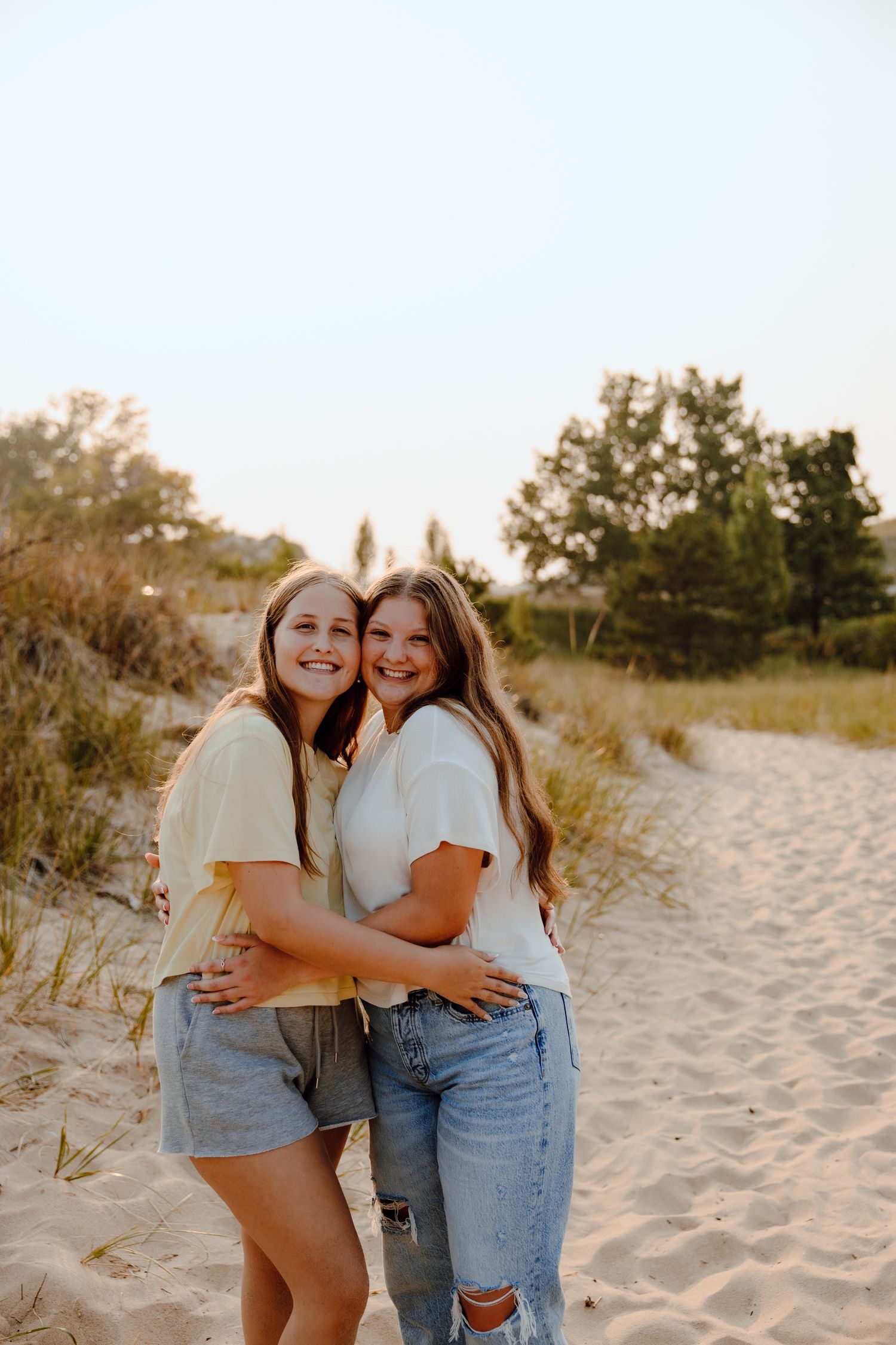Two friends embrace and laugh together on a sandy beach during golden hour.