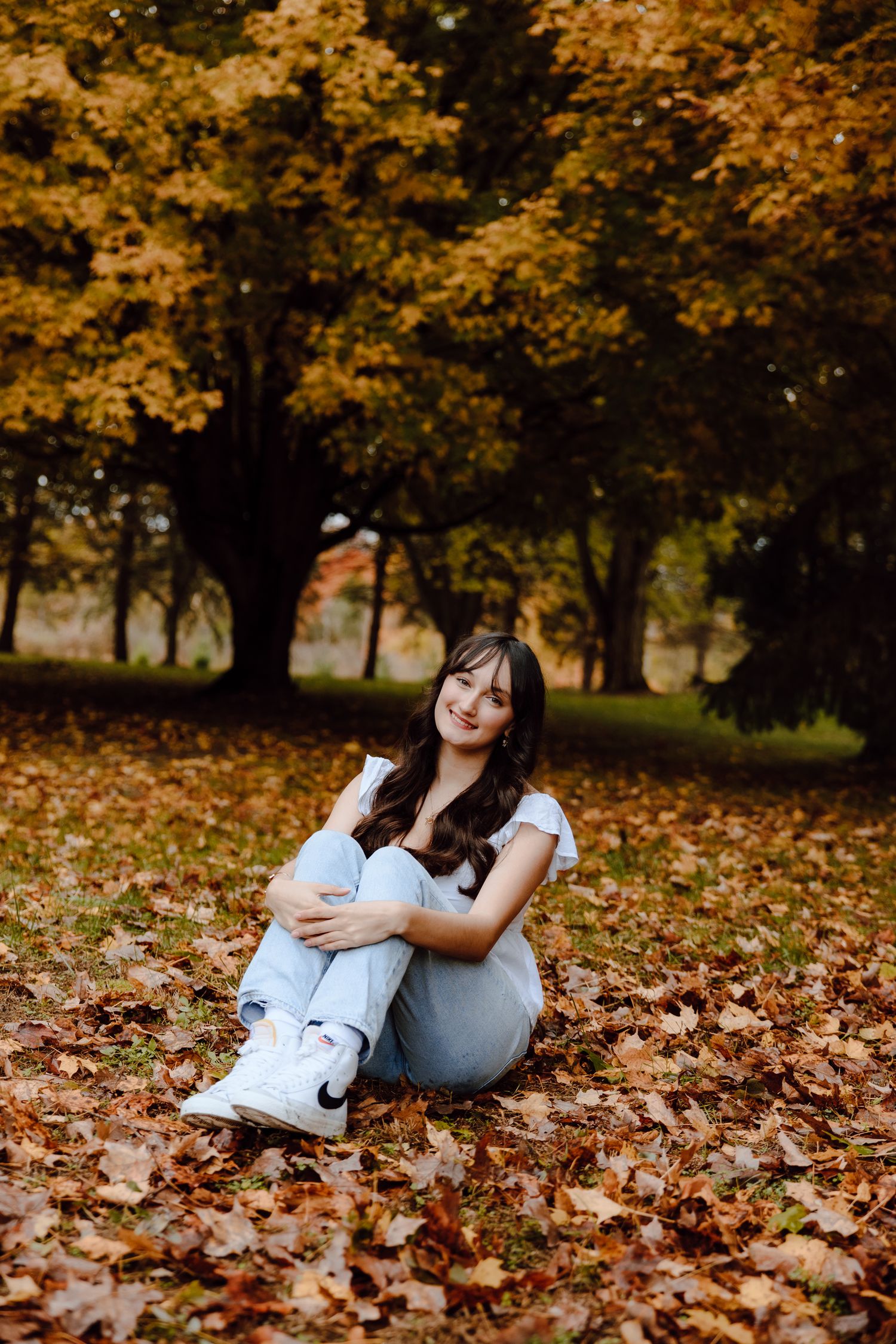 Casual outdoor portrait session among scattered fall leaves with trees in the background.