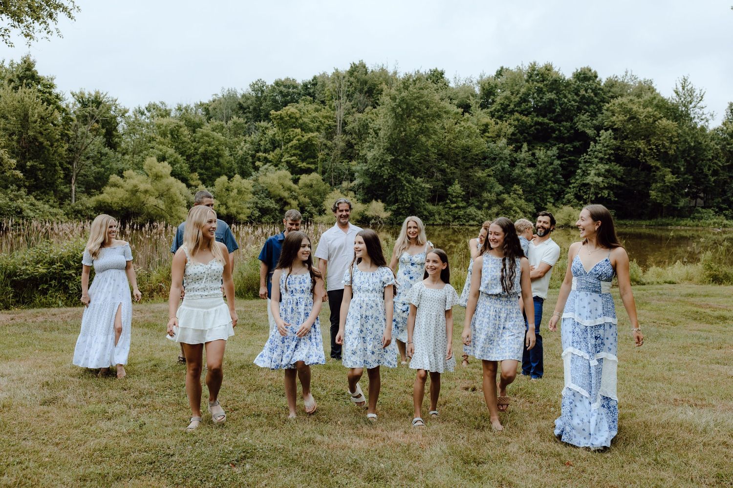 A group in coordinated blue and white dresses stands together in a grassy outdoor setting.