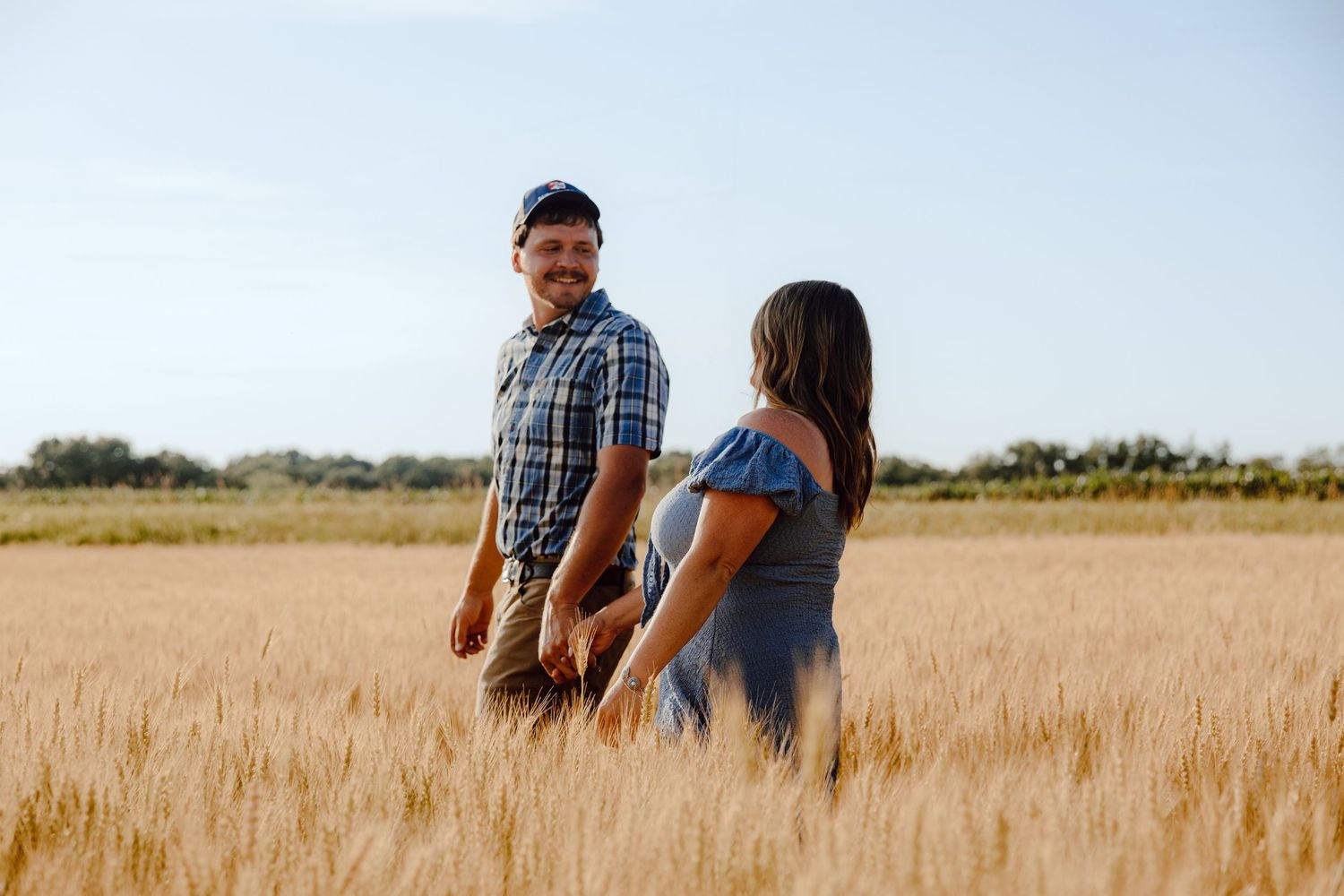 A couple dances playfully in a golden wheat field at sunset.