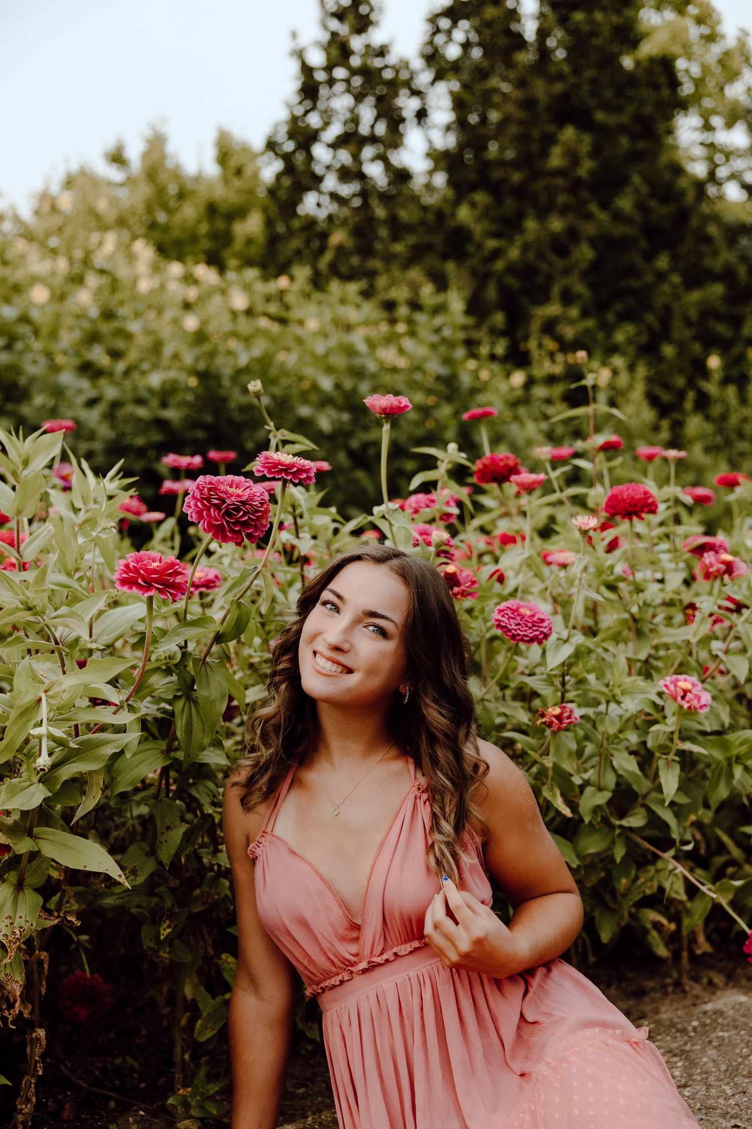 Portrait session in a pink dress among blooming red zinnias in a garden.