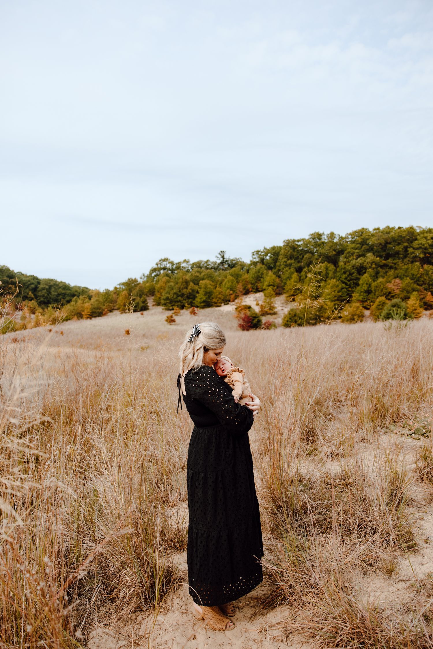 Two people share an intimate moment in a tall grass field surrounded by autumn foliage.
