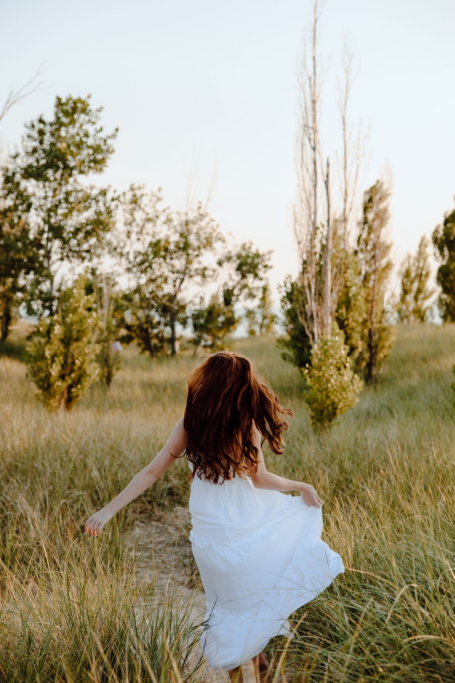 Someone in a white dress spins joyfully in a grassy field.
