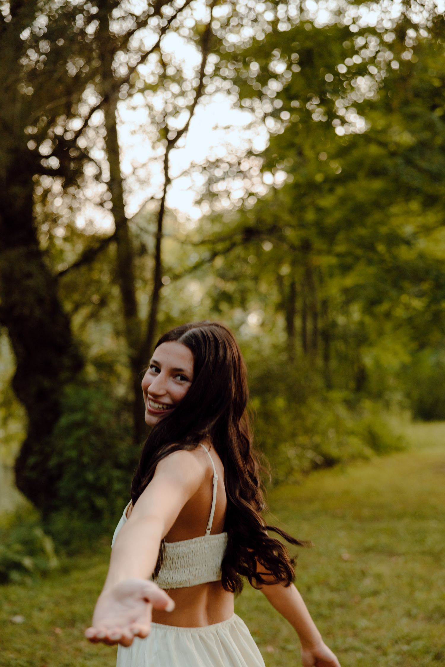 Playful outdoor photoshoot in a sunlit forest path with flowing dress.