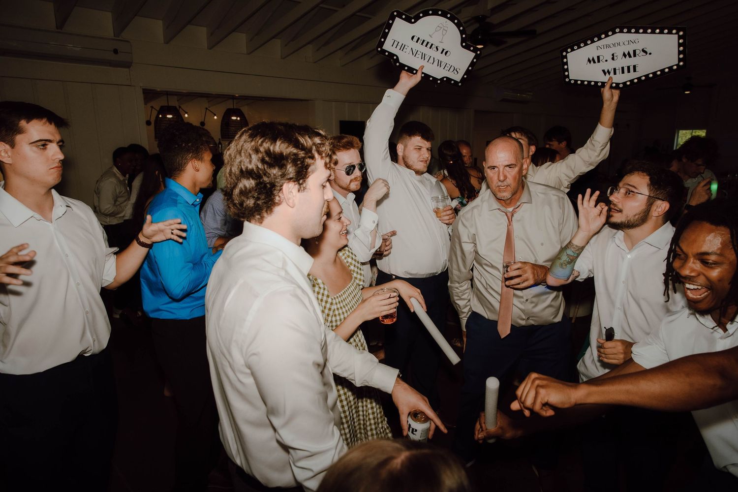 Lively wedding reception dance floor with guests holding photo booth signs and dancing together.