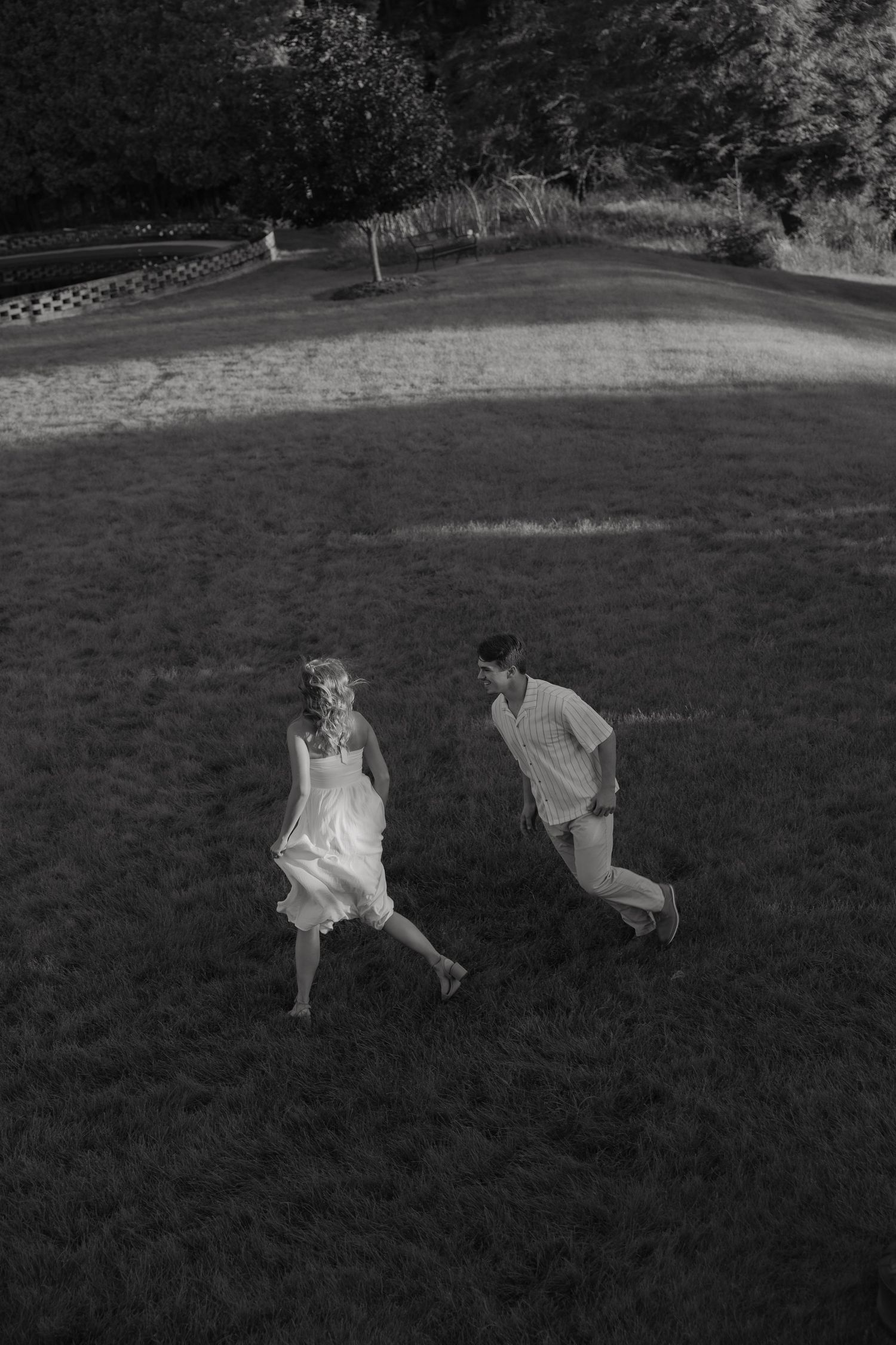 Black and white aerial photo of a couple running and laughing together across a lush green lawn.
