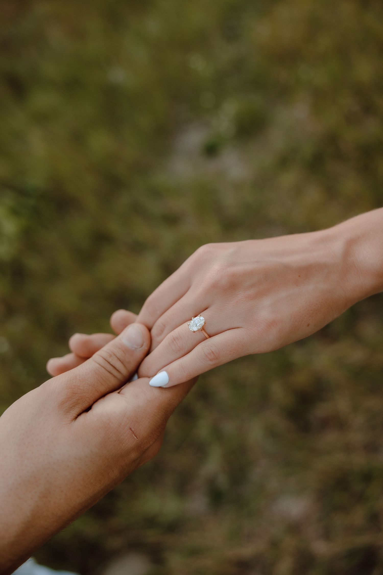 Close-up of a woman's hand wearing a pear-shaped diamond engagement ring held by her partner.