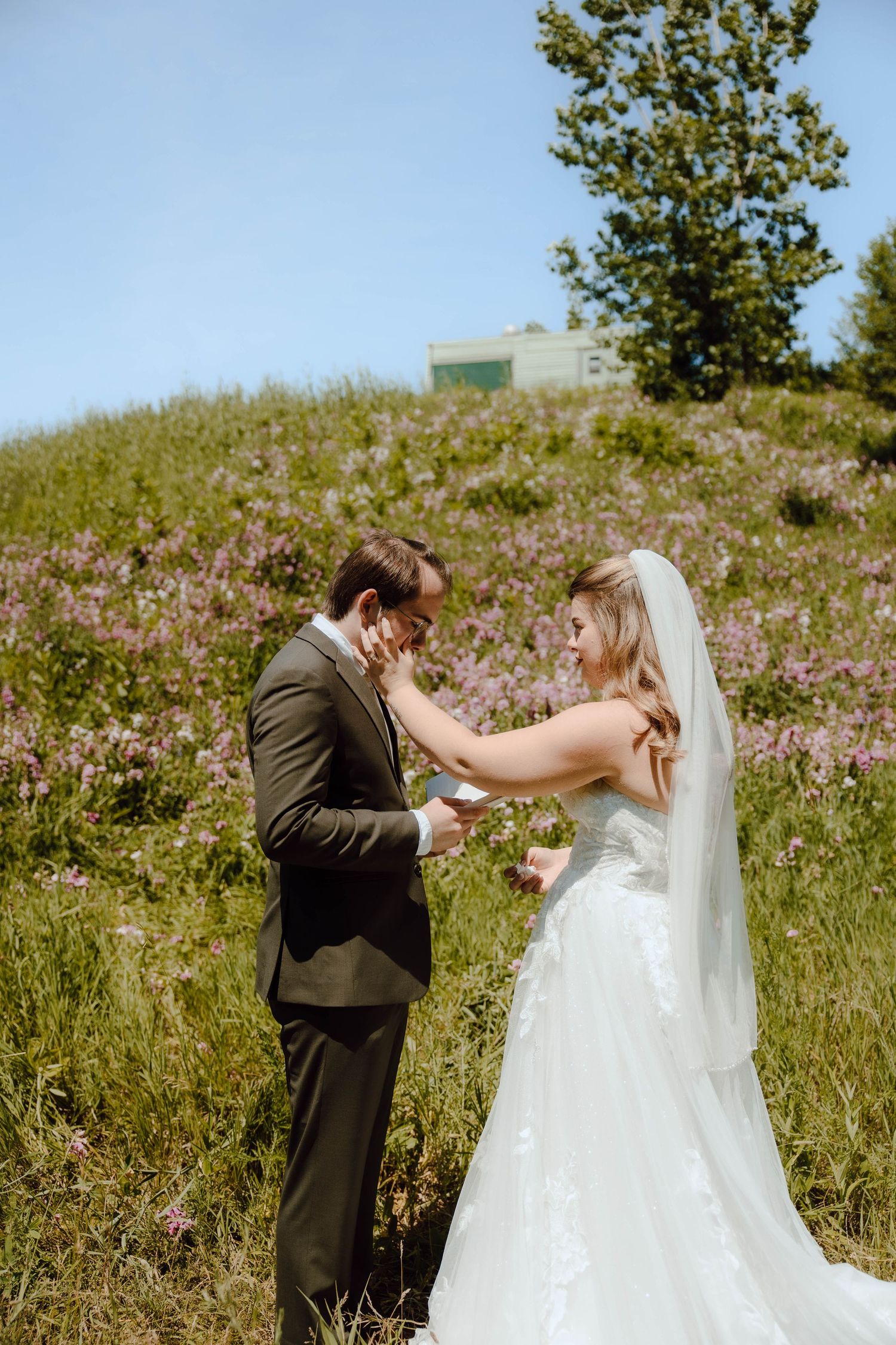 Bride and groom share tender first look moment in wildflower meadow on sunny wedding day.
