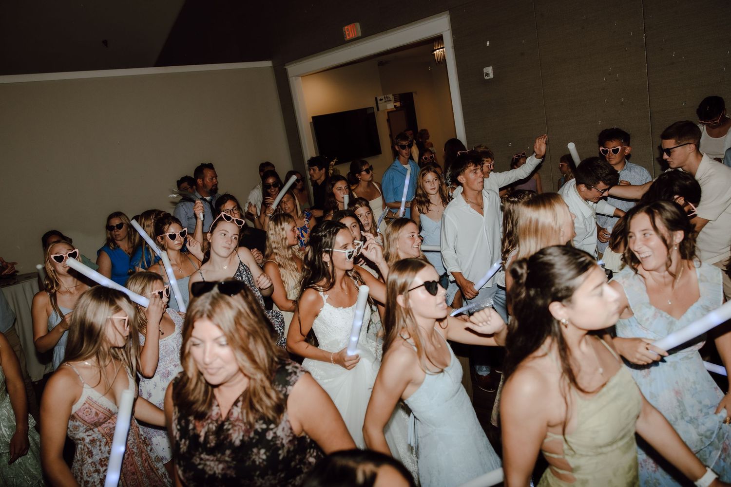 Large group of young people dancing and celebrating at an indoor party event with white decorations.