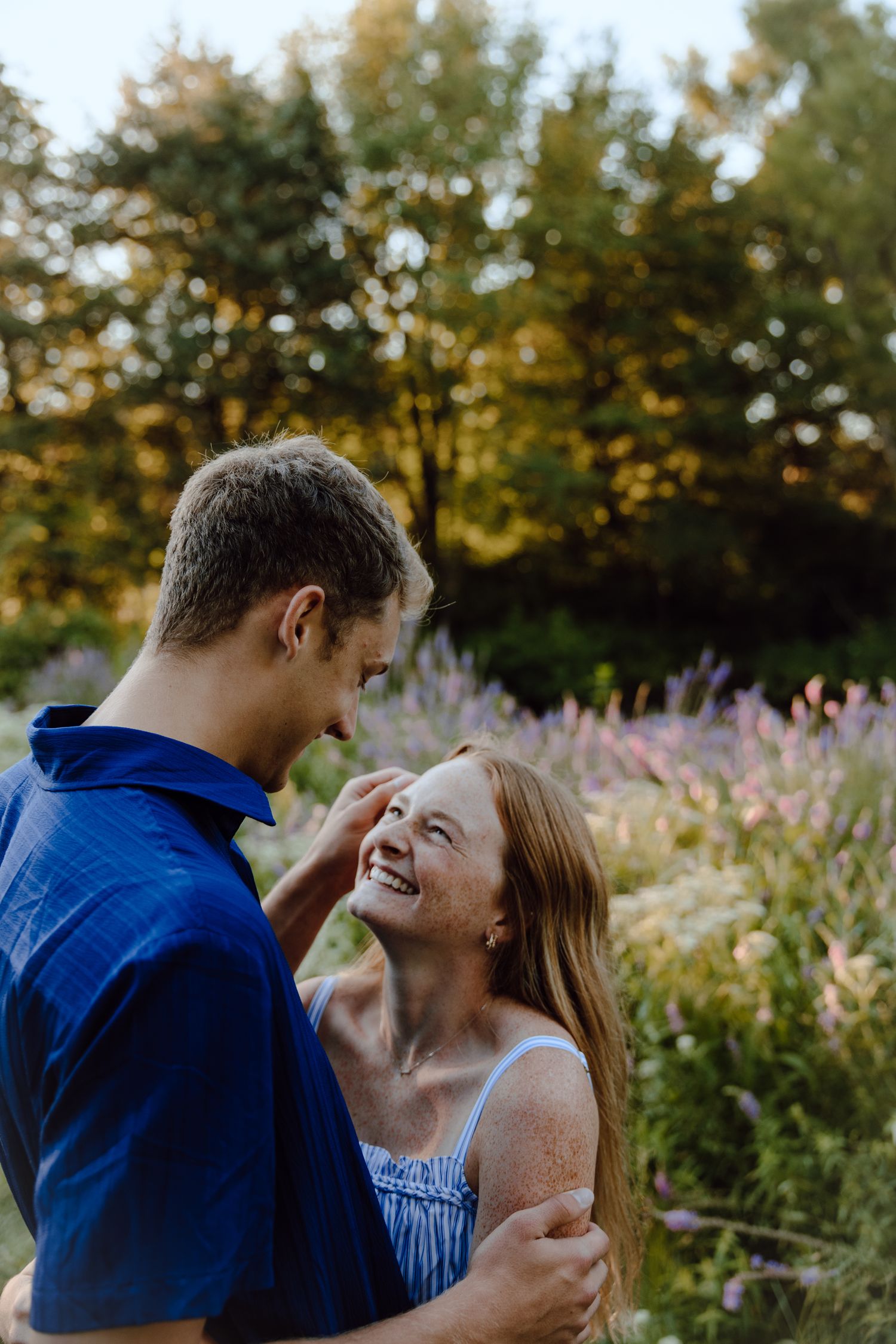 A couple shares a joyful moment together in a garden filled with purple wildflowers at sunset.